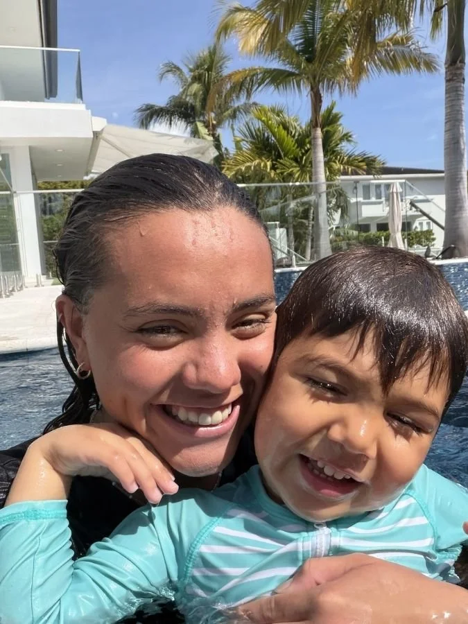 Swimming coach Alex smilling, holding a young swimming student inside the pool.