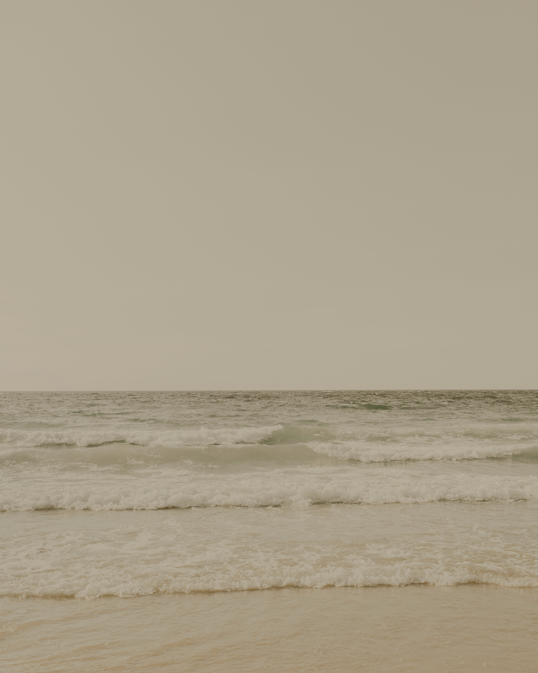 A calm beach with gentle waves rolling onto the sandy shore under a cloudy sky.