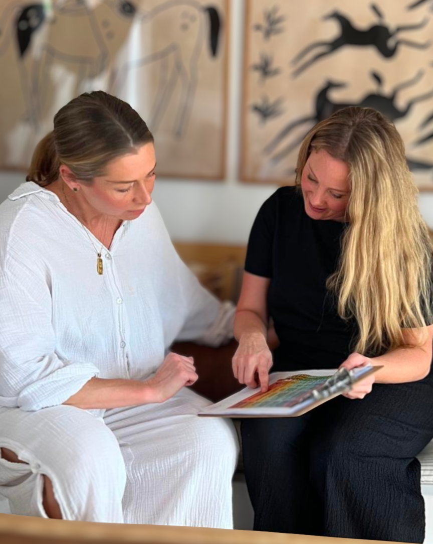 Two women sitting together, looking at a Spinal Flow color chart or palette, in a room with abstract wall art in the background.