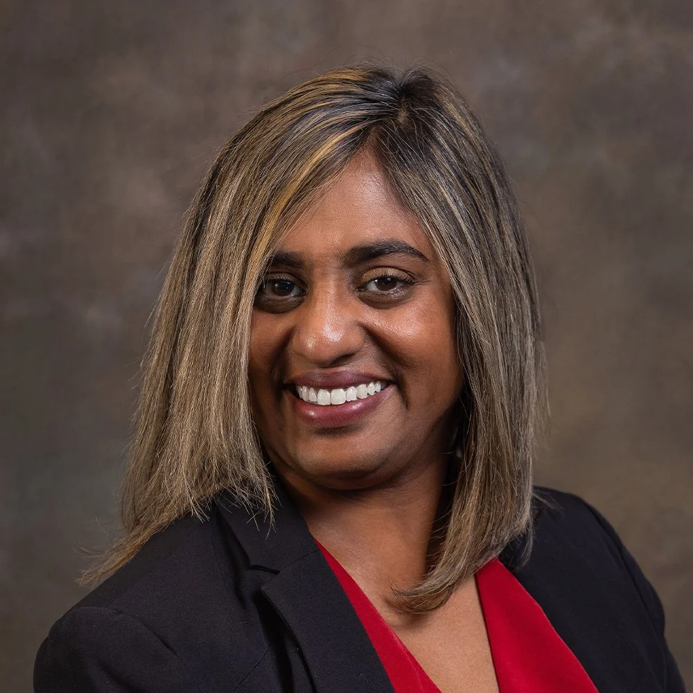 A woman with shoulder-length hair smiling, wearing a black blazer over a red top.