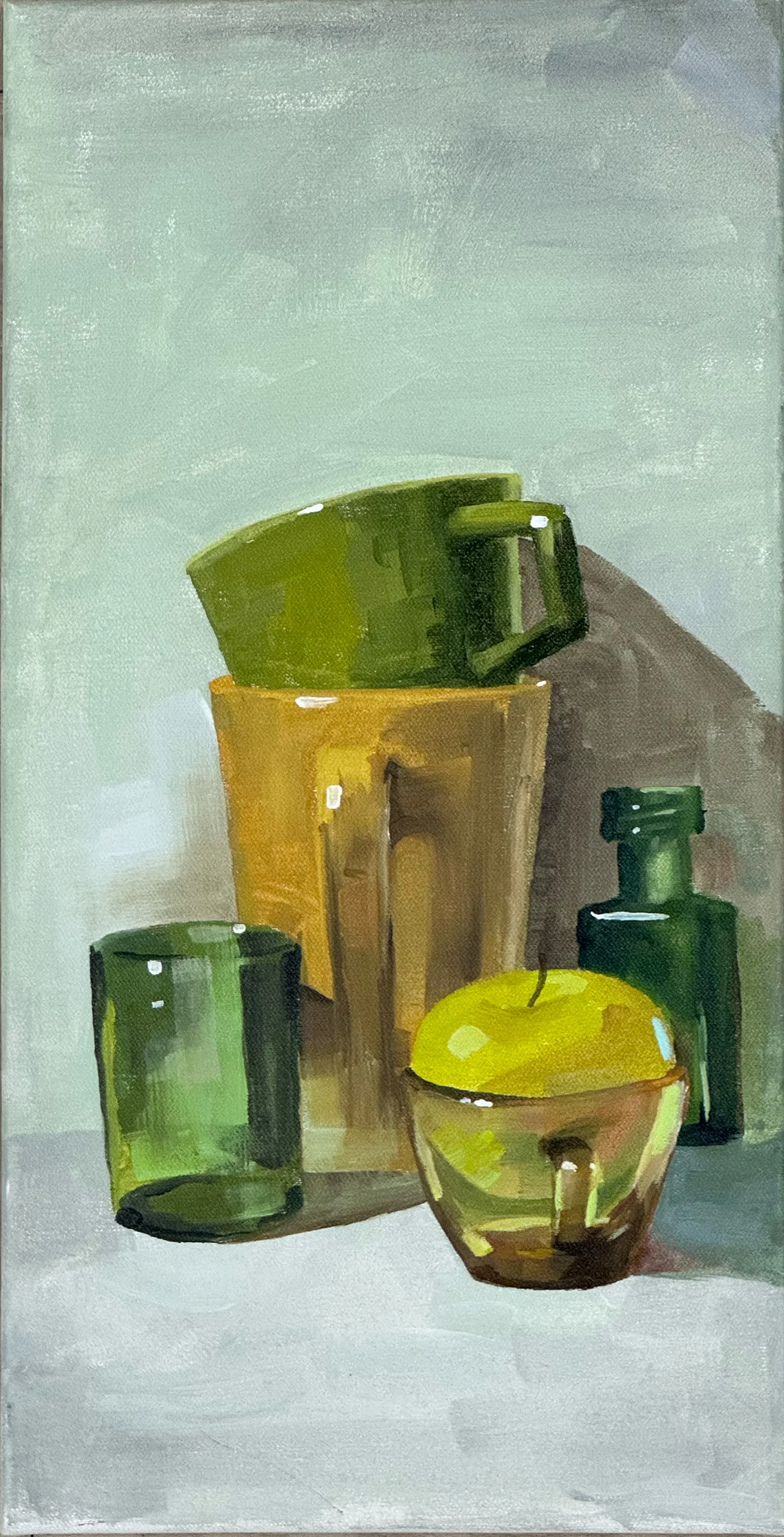 Stillleben mit grünen und braunen Keramiktassen, einem grünen Glas, einer grünen Flasche und einem gelben Apfel auf einem weißen Untergrund.