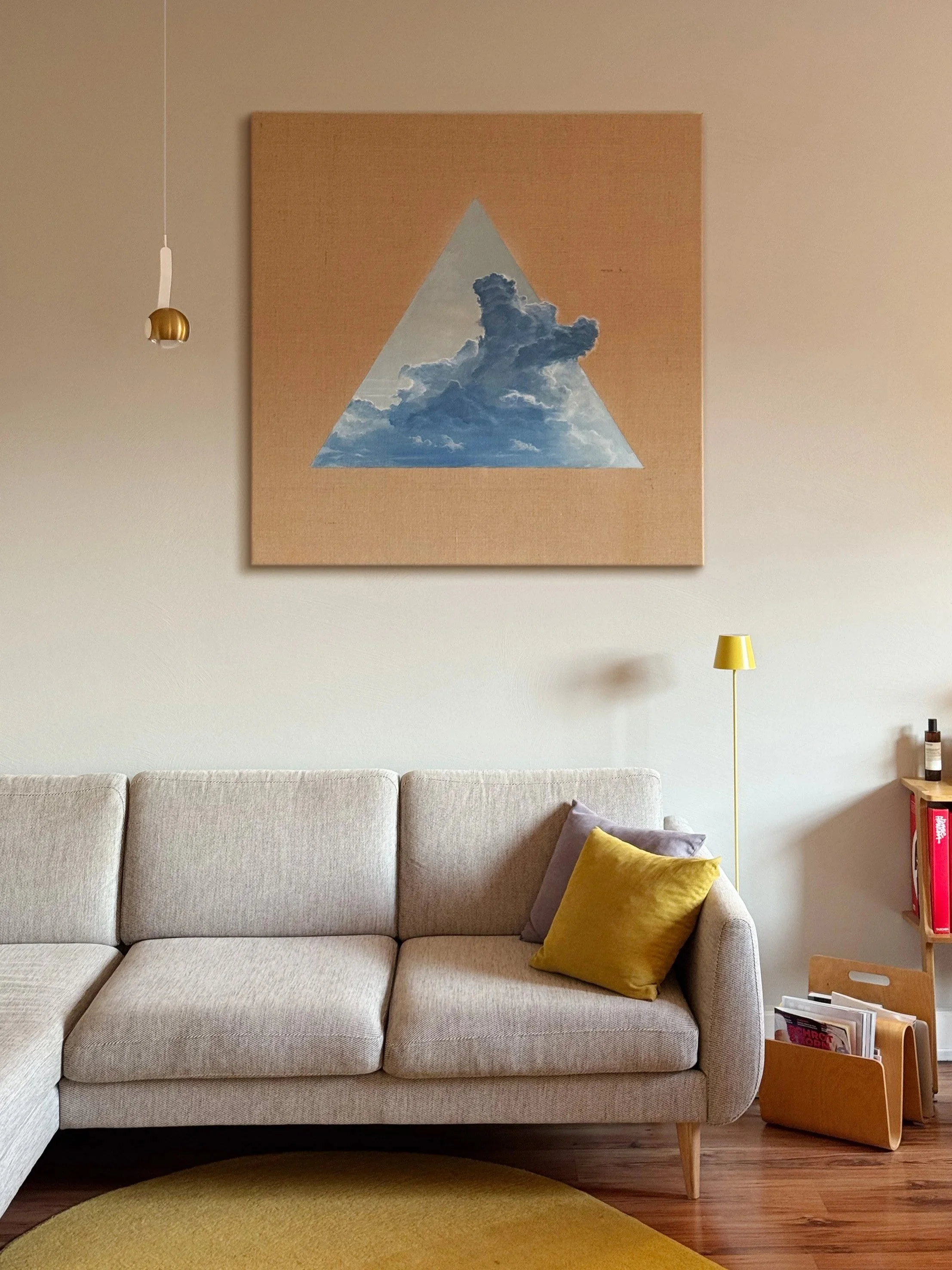 Ein modernes Wohnzimmer mit einem beige Blumenstoff Couch, mehreren Kissen, einer Stehlampe, einem Bilderrahmen an der Wand und einem Regal mit Magazinen.