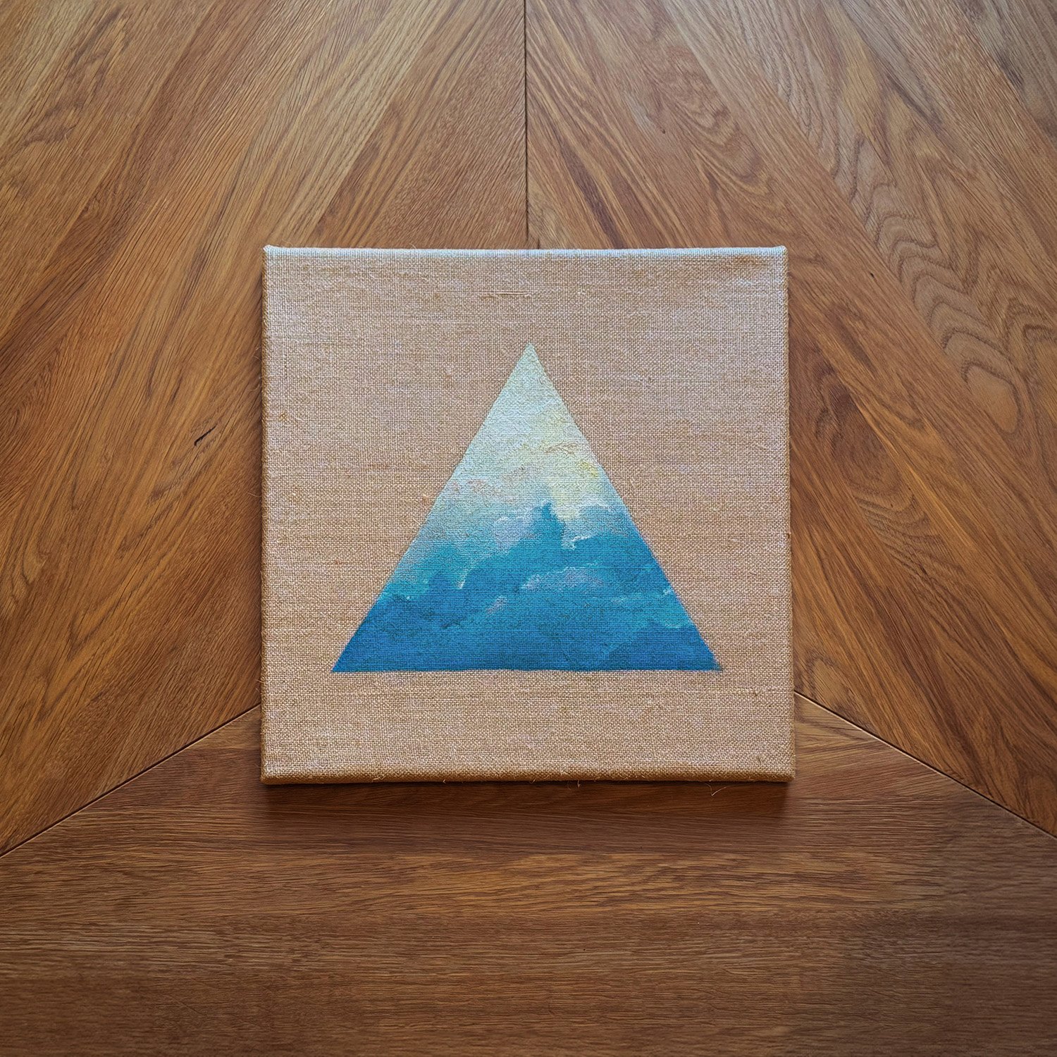 Querformatige Leinwand mit einem blauen im Himmel schwebenden Dreieck, auf einem Holzfußboden