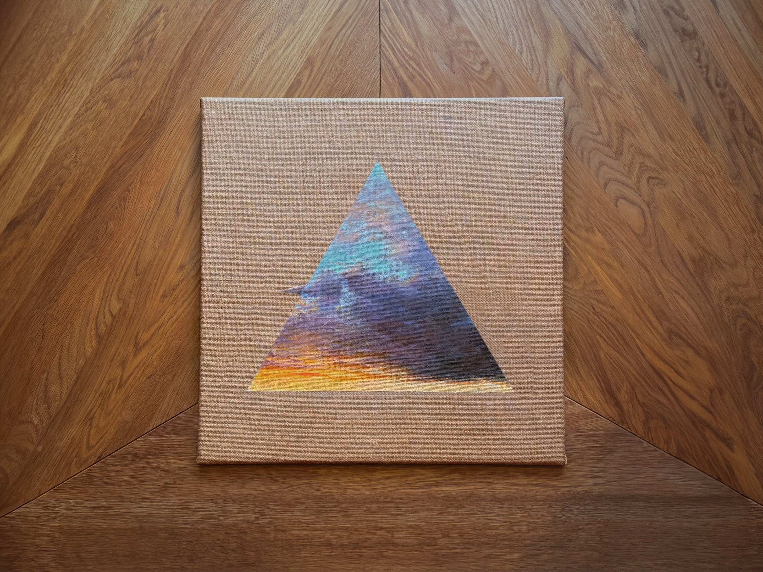 Gemälde mit einem Berg und einer Wolke, in einem Dreieck auf einem Leinwandstoff, auf einem Holztisch.