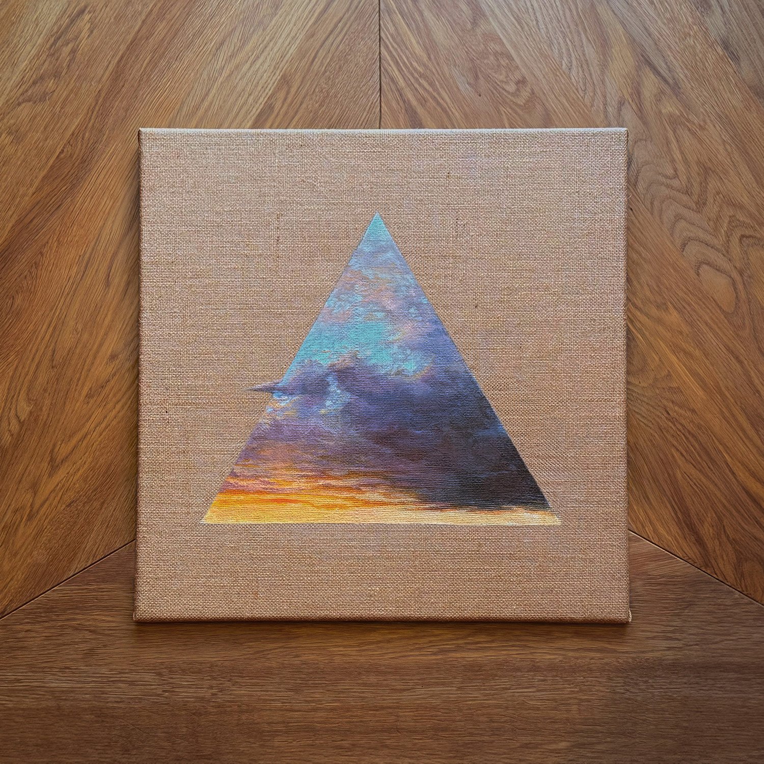 Ein Gemälde, das eine bunte Wolkenformation in einem Dreieck zeigt, auf einem Holztisch.