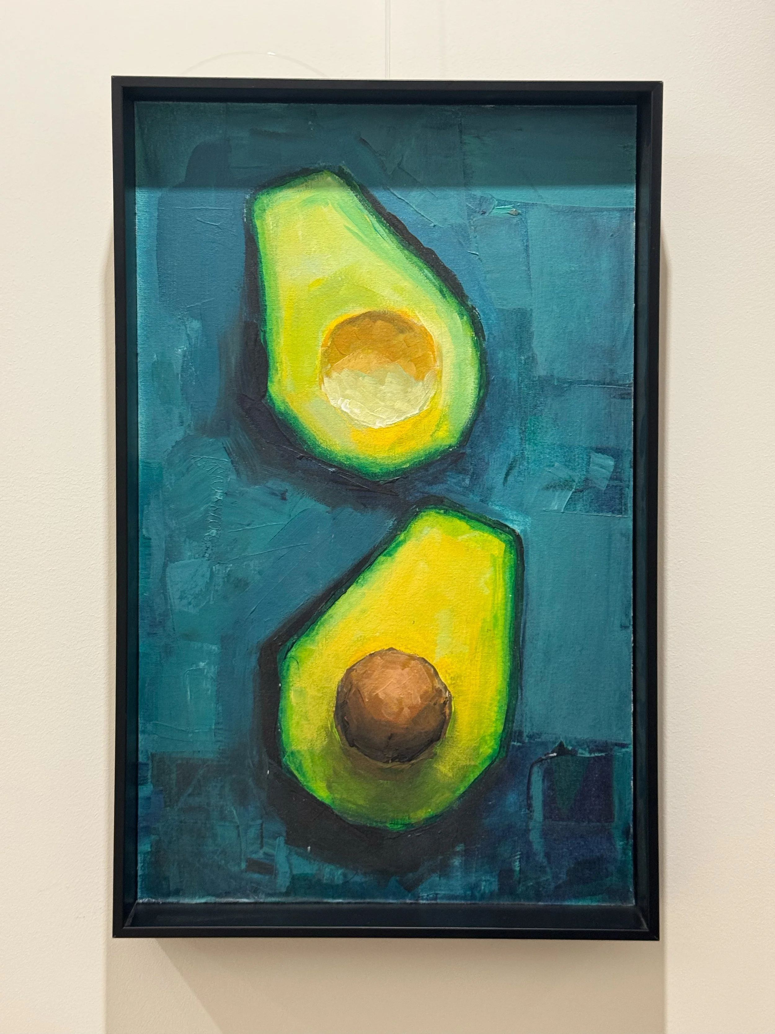 Ein Gemälde mit zwei aufgeschnittenen Avocados, eine mit grünem Fruchtfleisch und einem braunen Kern, die andere mit einem braunen Kern, auf einem blauen Hintergrund.