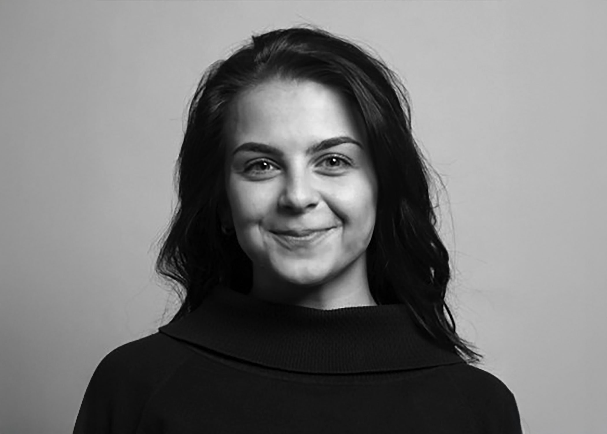 Black-and-white portrait of a woman with wavy dark hair, smiling, wearing a dark top with a wide collar, against a plain background.