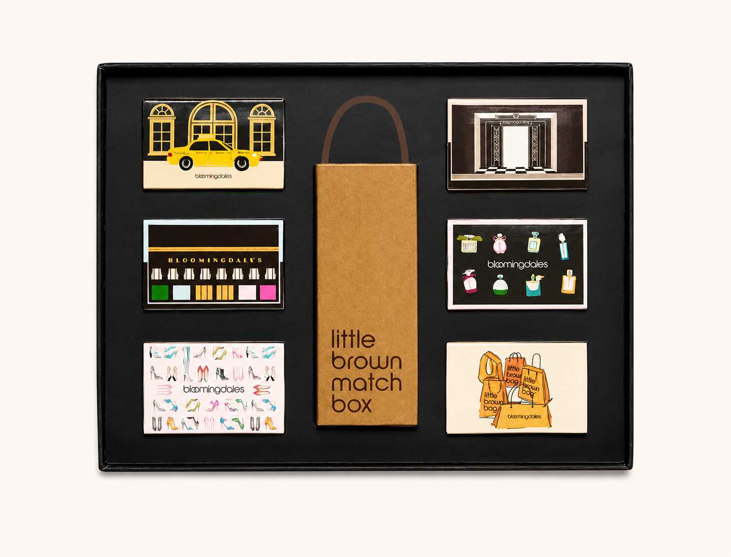 A collection of various small boxes and cards with colorful illustrations and designs, arranged in a grid inside a black presentation box. In the center, there is a brown box with the words 'little brown match box.'