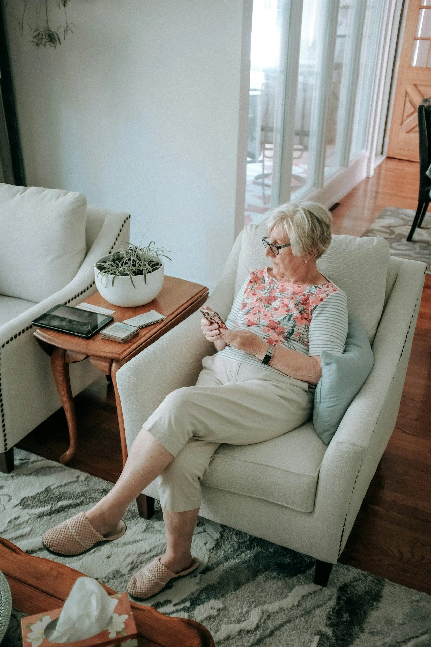 elderly woman sitting in an armchair, scrolling through her phone