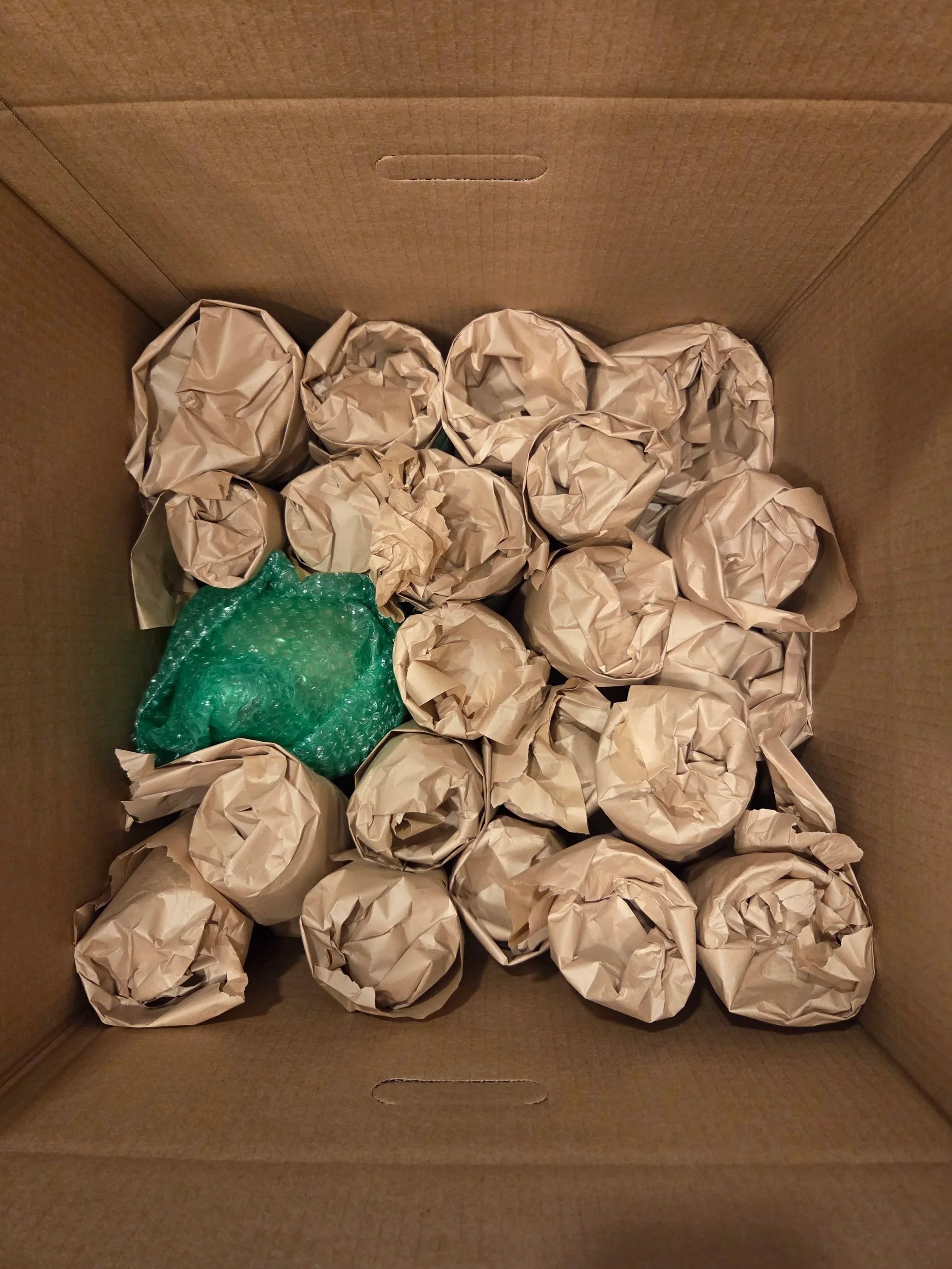 Image shows glassware which has been individually wrapped in protective paper and bubble wrap, and carefully packed inside a moving box