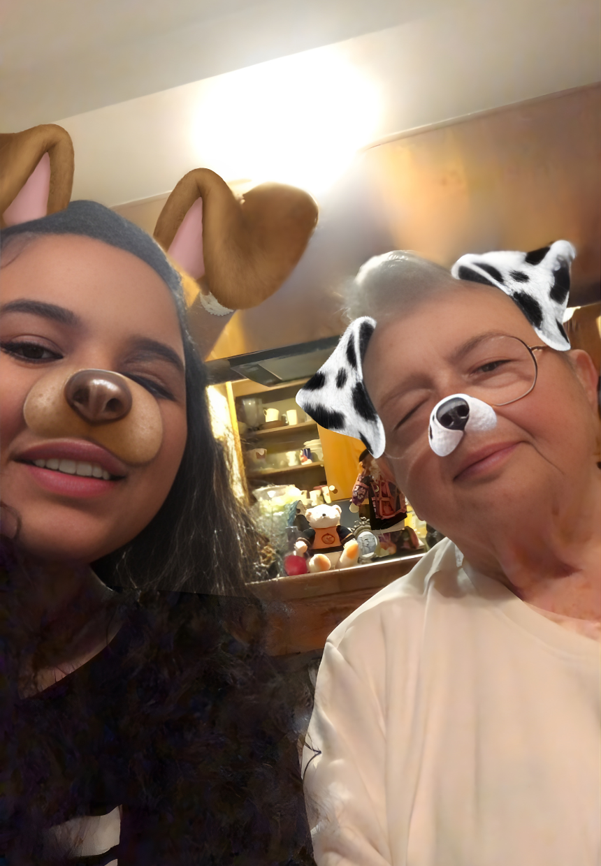 Two people taking a selfie with dog filter and bunny filter. Both are smiling, indoors with warm lighting and shelves in the background.