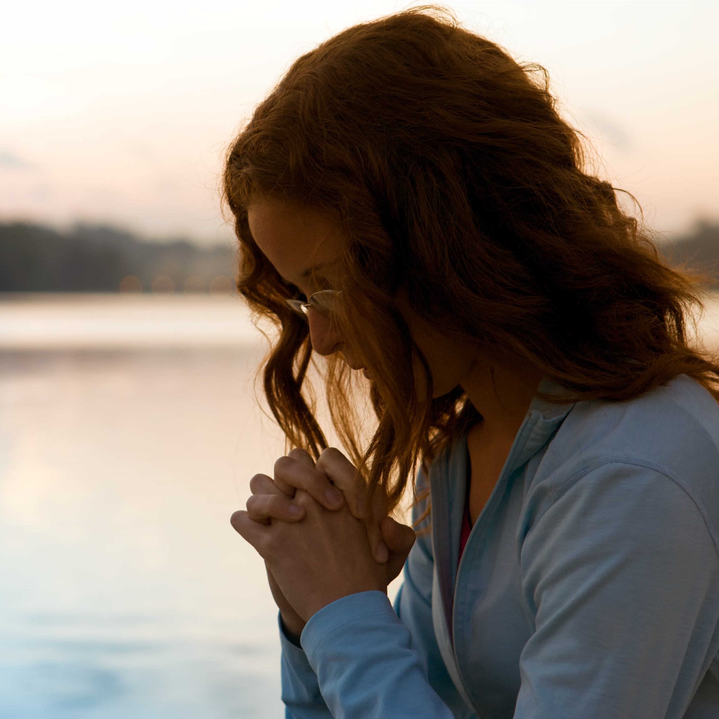 A silhouetted woman bows her head and clasps her hands in prayer