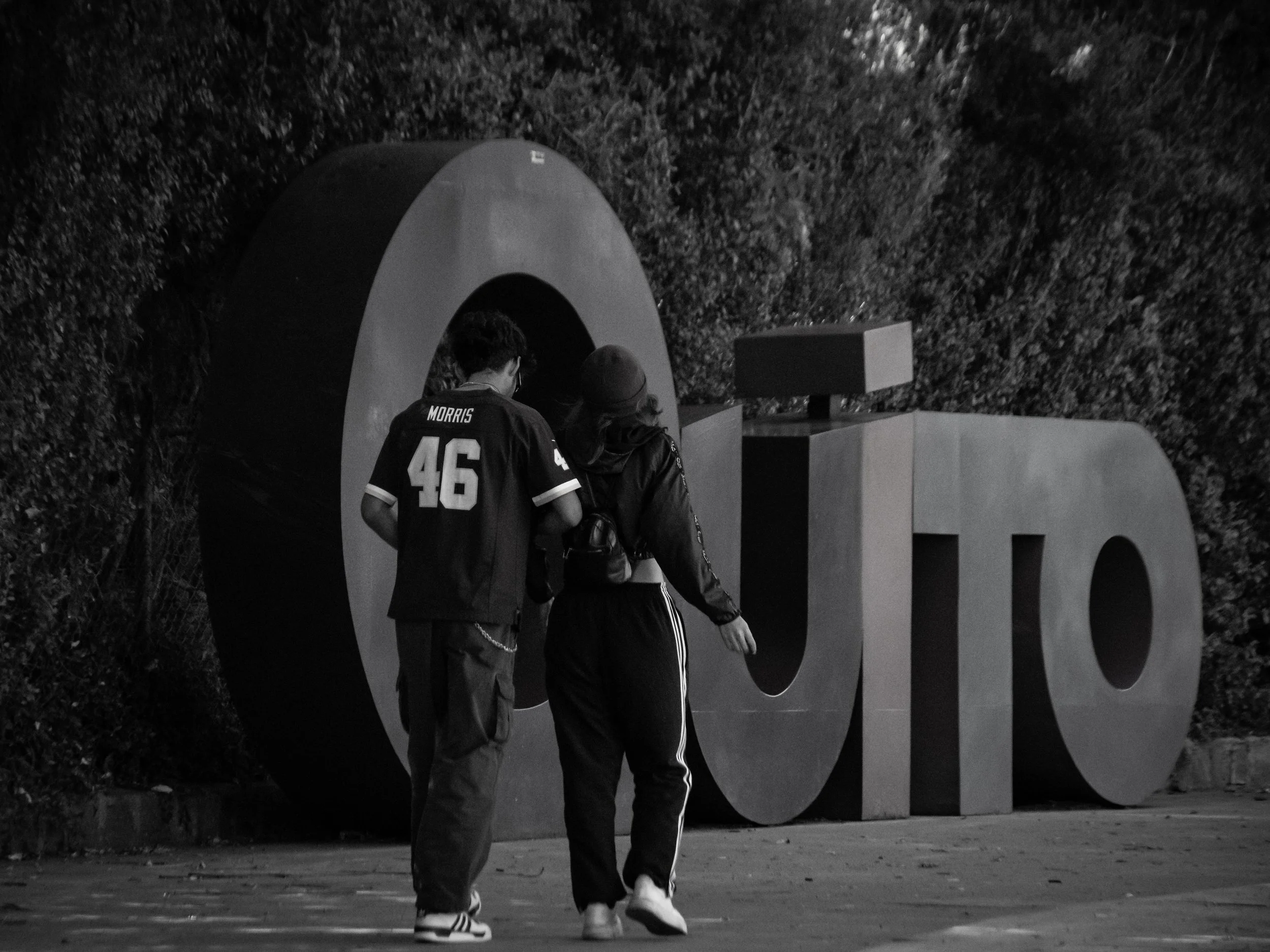 Two people walking past a large 3D sculpture of the word 'LOVE' at night, with a background of trees.