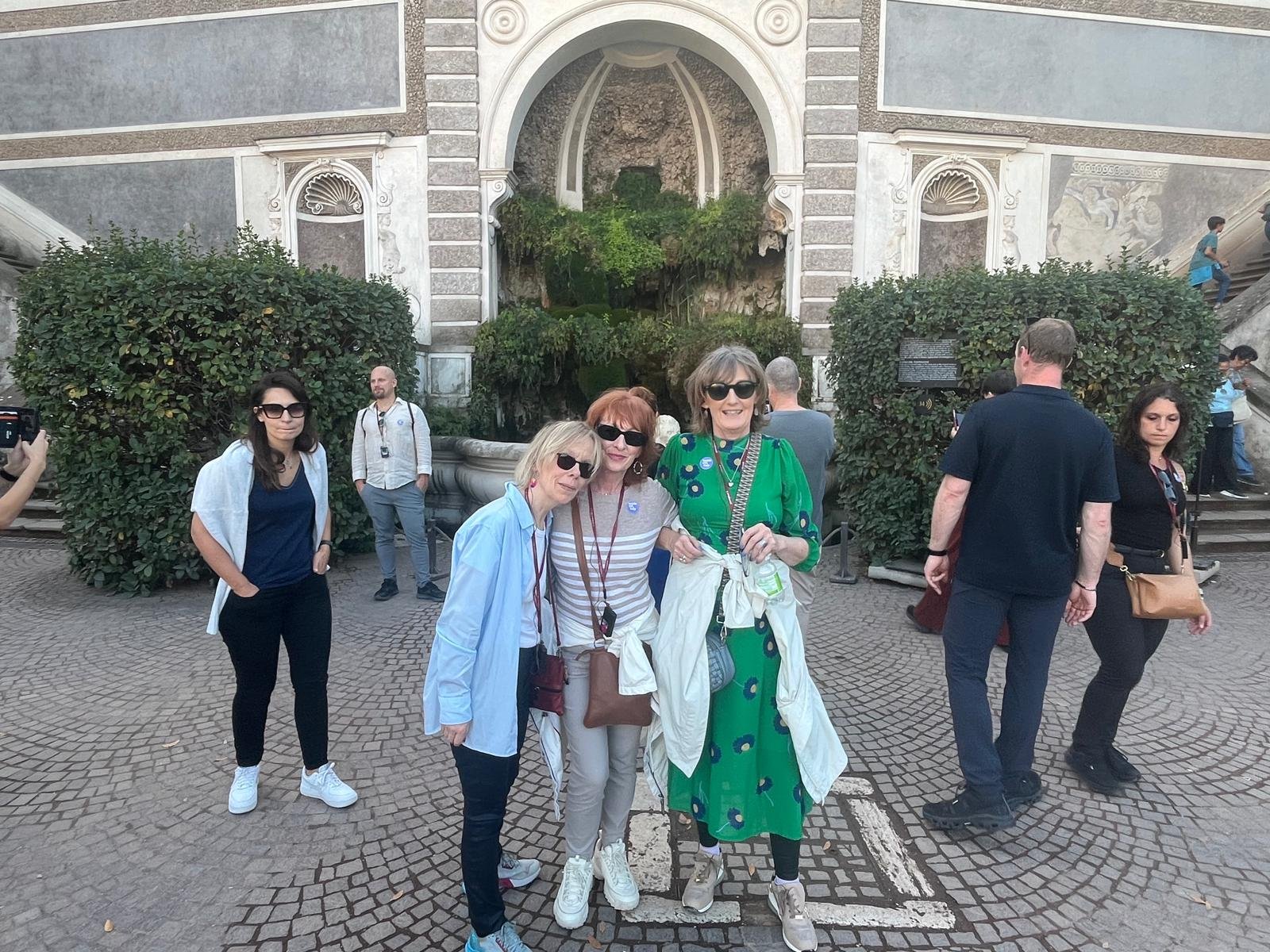 Breda and friends standing in front of a historic fountain and ornate building, with some people taking photos and others posing for pictures.