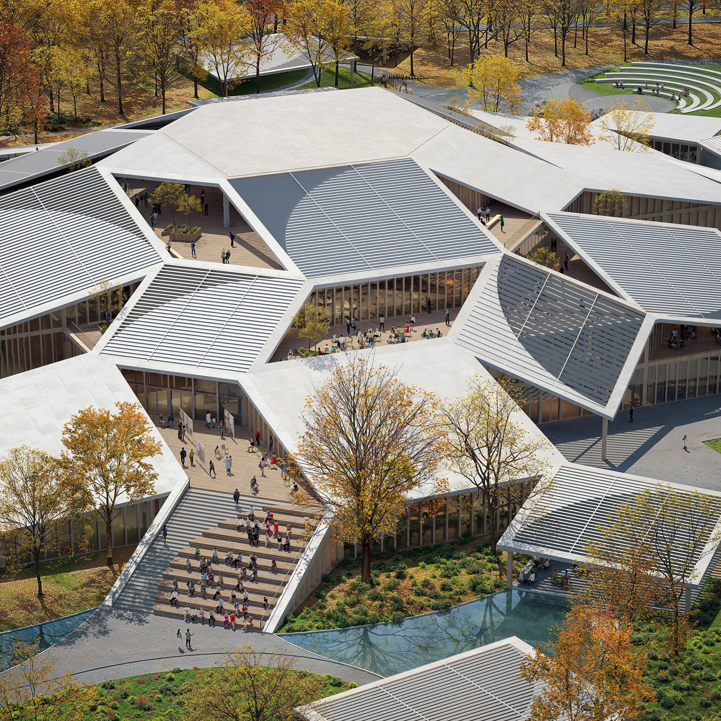 Aerial view of a modern building with geometric, angular rooftops and outdoor gathering areas, surrounded by trees with autumn foliage.