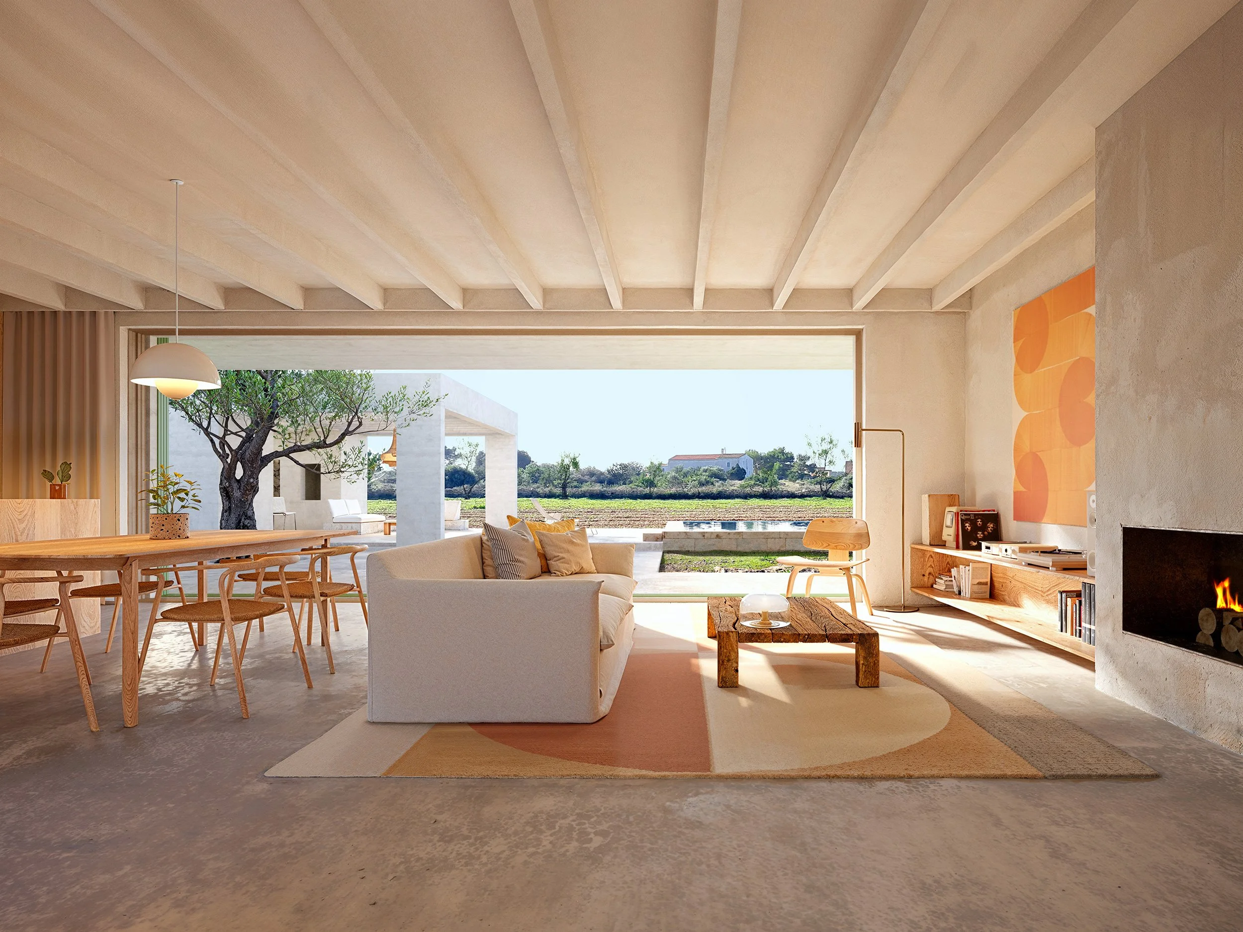 Modern living room with large open window, white sofa, wooden coffee table, colorful abstract wall art, fireplace, and outdoor view of landscape and trees.