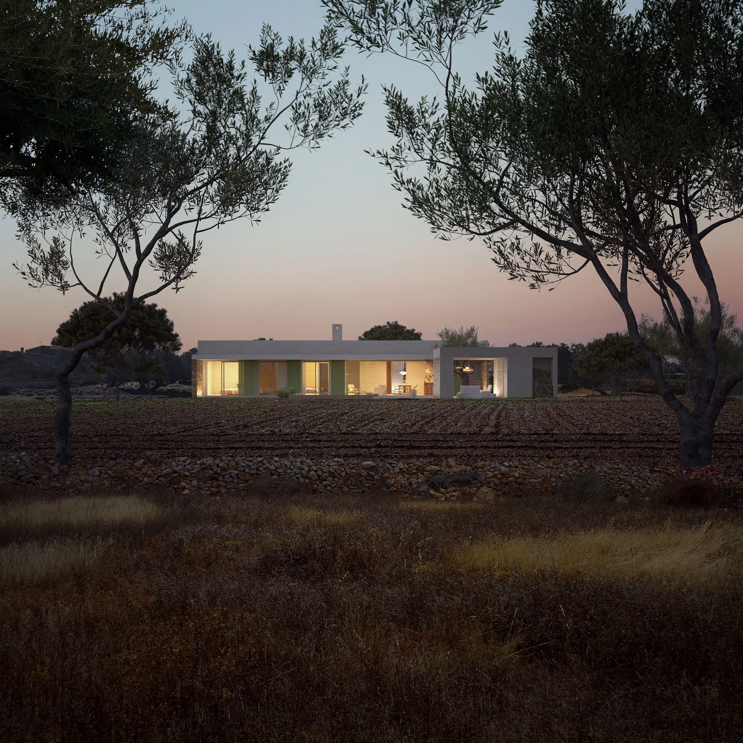 A modern single-story house illuminated from the inside, situated in a rural landscape with trees in the foreground at dusk.