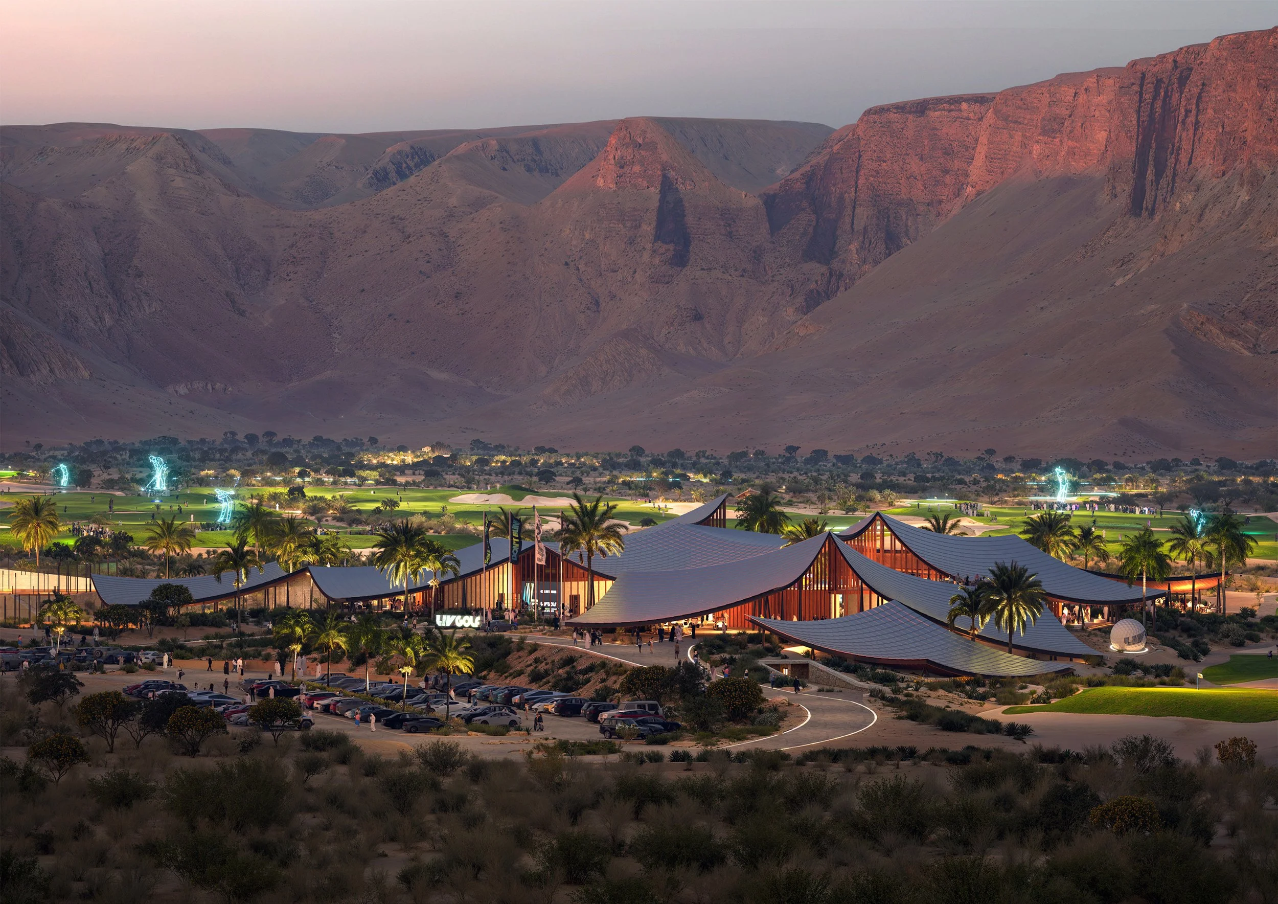 Night view of a modern building with curved rooflines, palm trees, and parked cars in a desert landscape with mountains in the background.