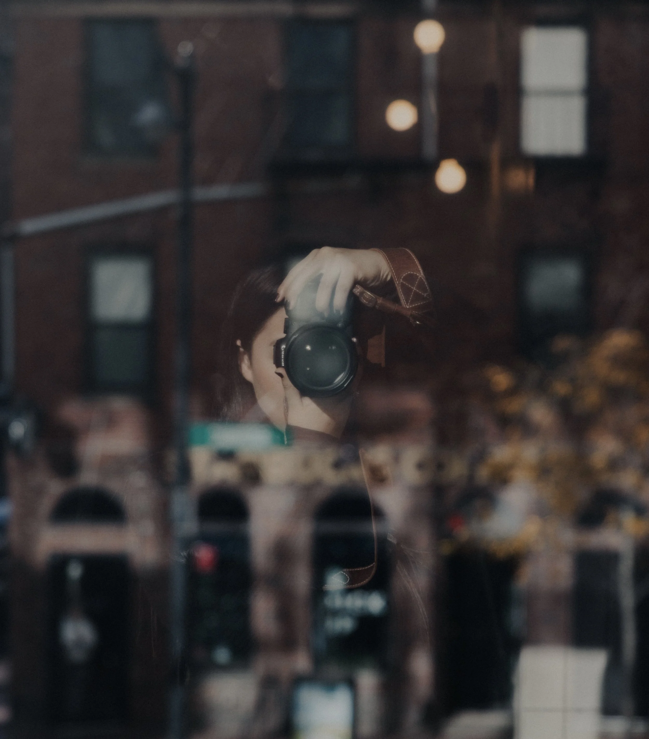 Reflection of a person taking a photo with a camera, seen through a glass window with small circular lights and blurred background.