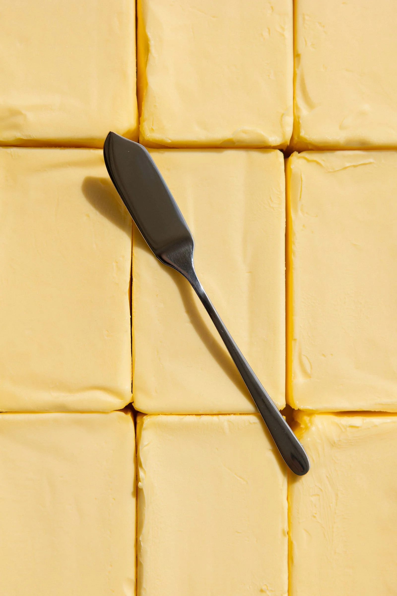 Close-up of yellow butter blocks on a surface with a butter knife.