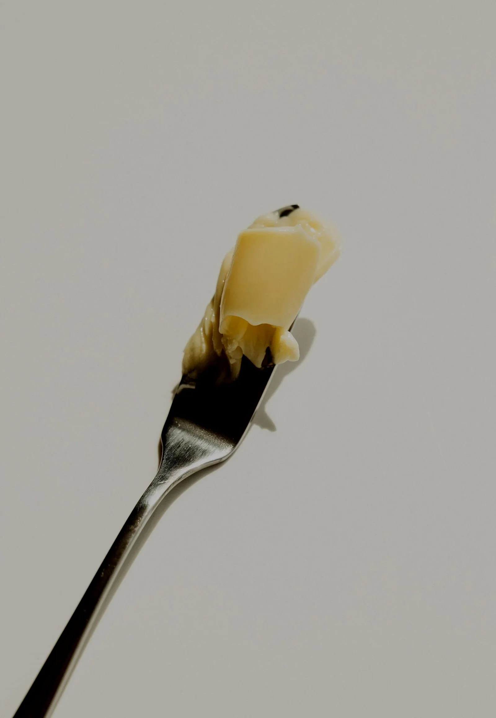 Piece of white chocolate with black specks on a silver fork against a plain white background.