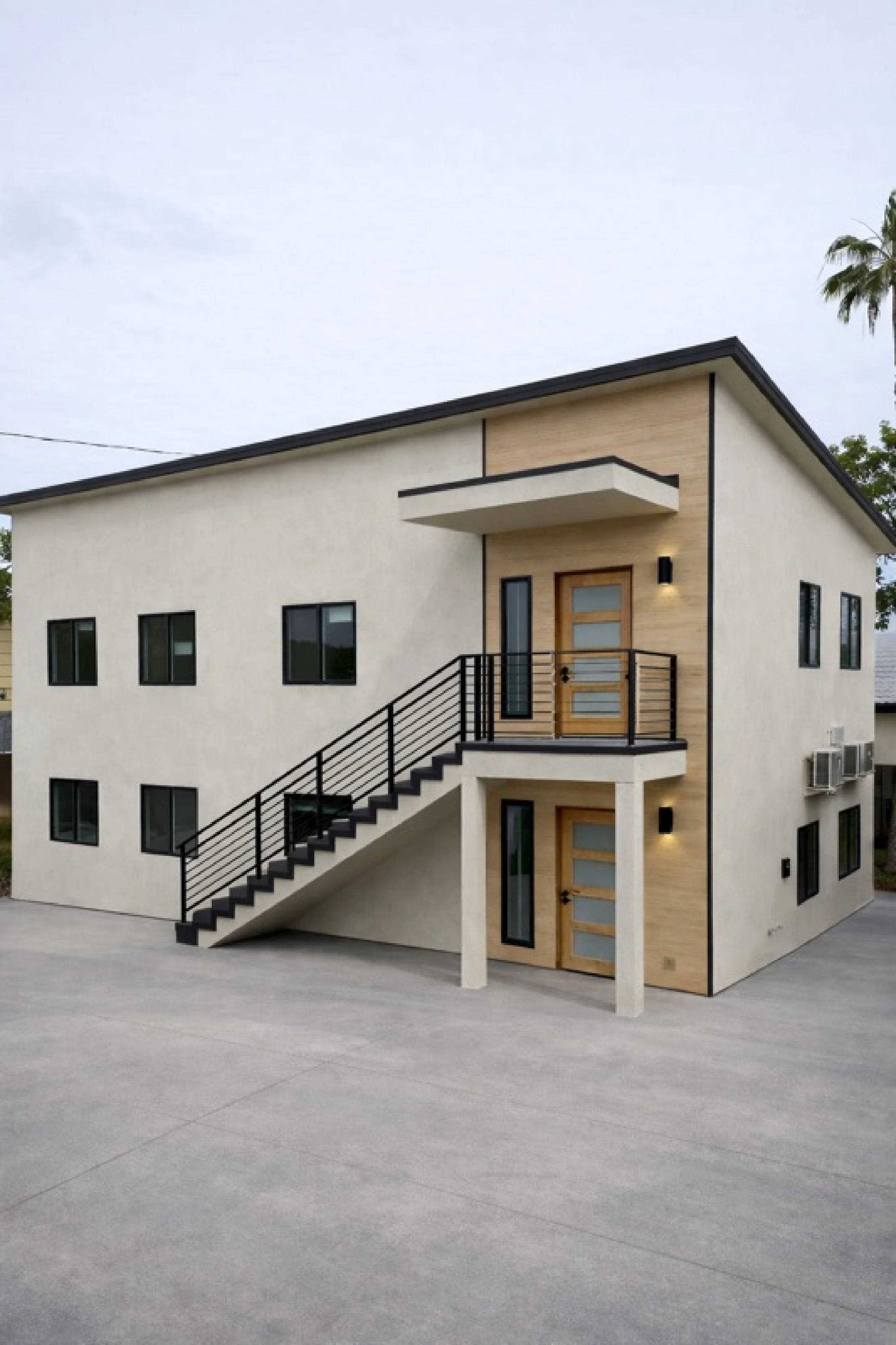 Modern two-story house with beige exterior, black metal staircase, and wooden doors, located on a concrete driveway.