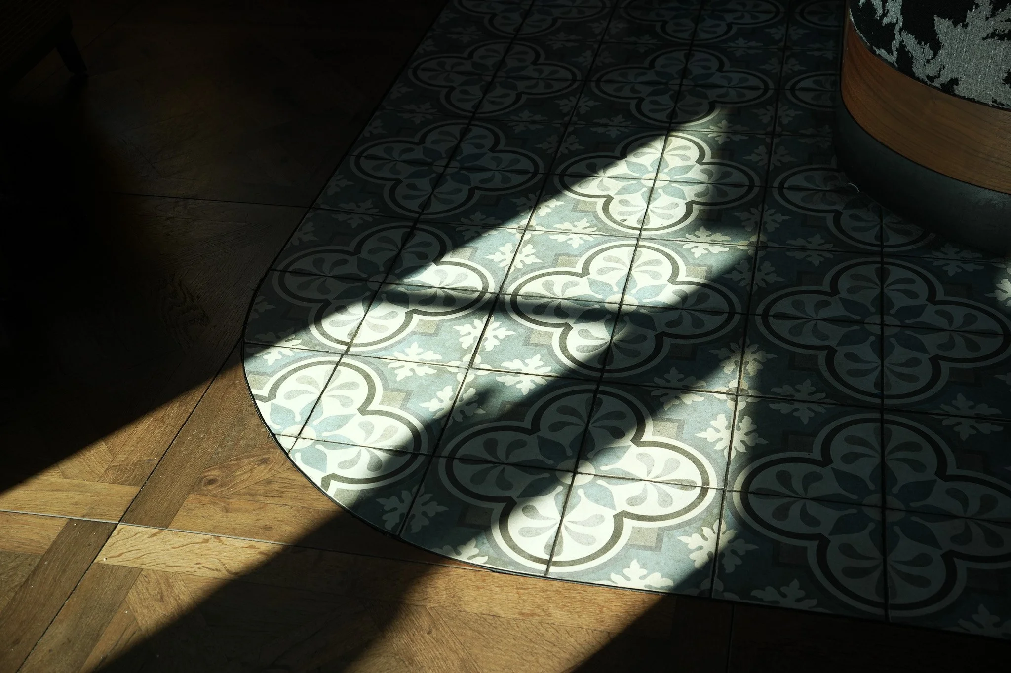 Sunlight casts shadows on a patterned tile and wooden floor.