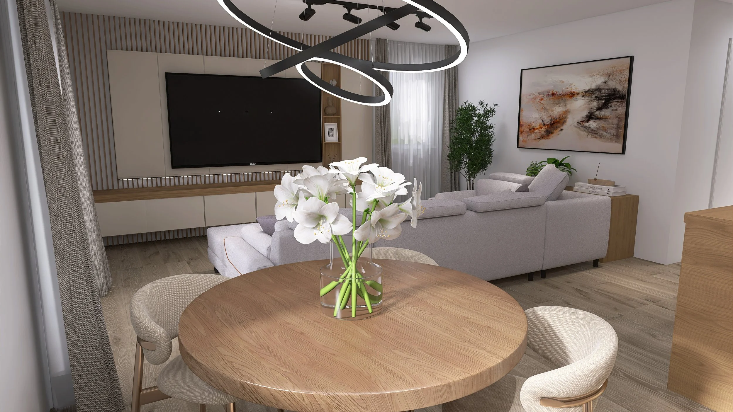 Modern living room with a round wooden dining table, white flowers in a glass vase, beige chairs, a large gray sectional sofa, a large flat-screen TV, artwork on the wall, and a window with sheer curtains.