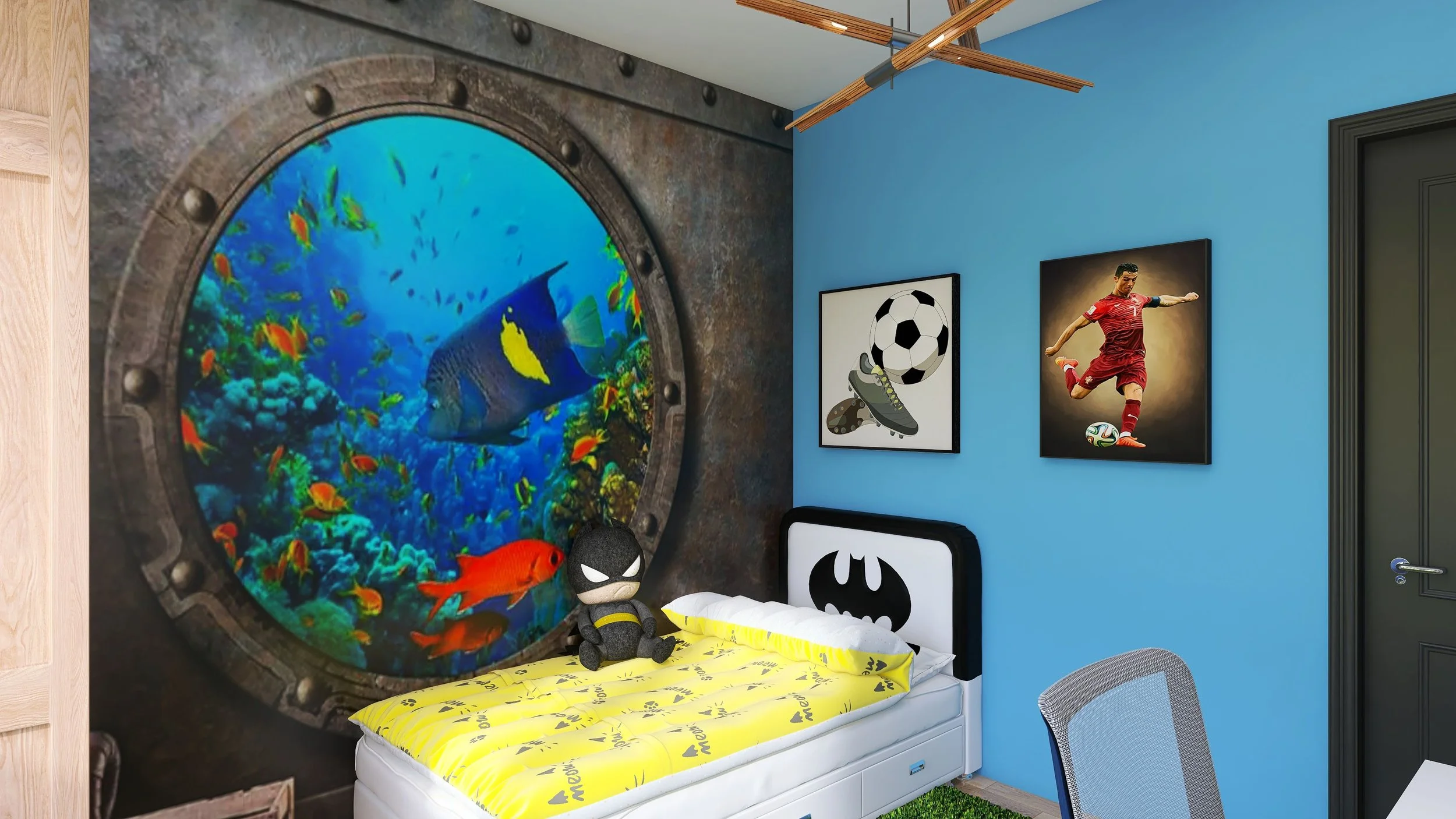 A bedroom with a porthole window showing an underwater scene with colorful fish and a fish with a yellow tail. The bed has Batman-themed bedding, a plush Batman toy, and framed sports-themed artwork on the blue wall. There is a gray mesh desk chair and a dark gray door.