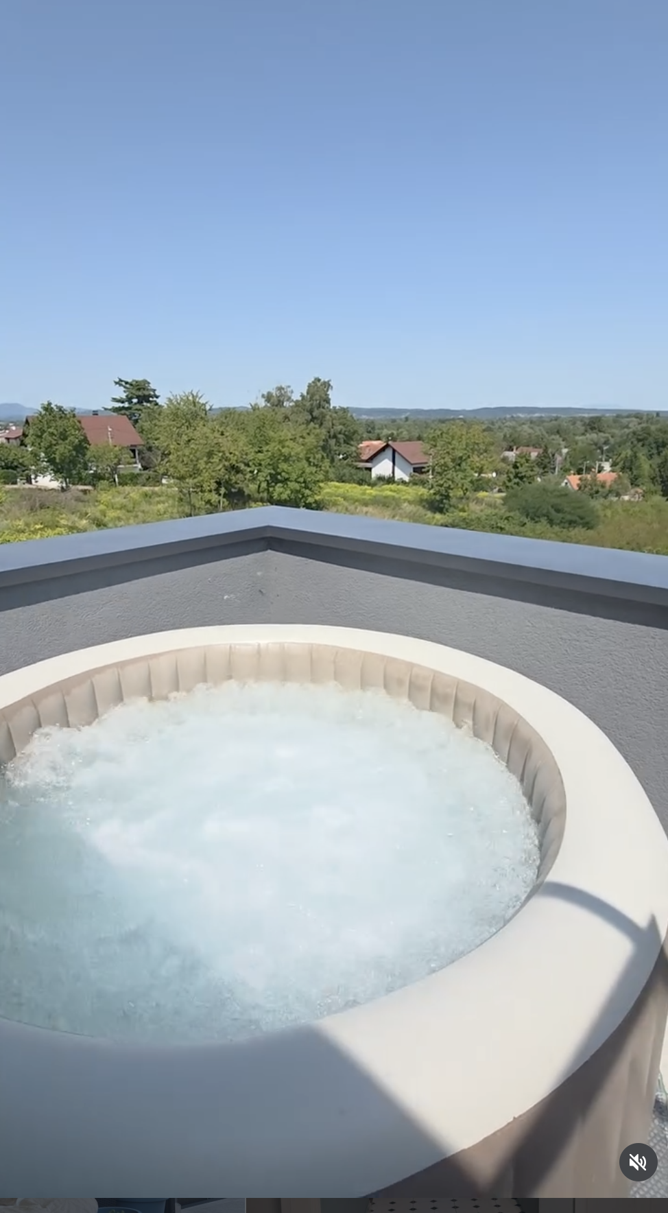 A hot tub on a balcony with a view of houses, trees, and a blue sky in the background.