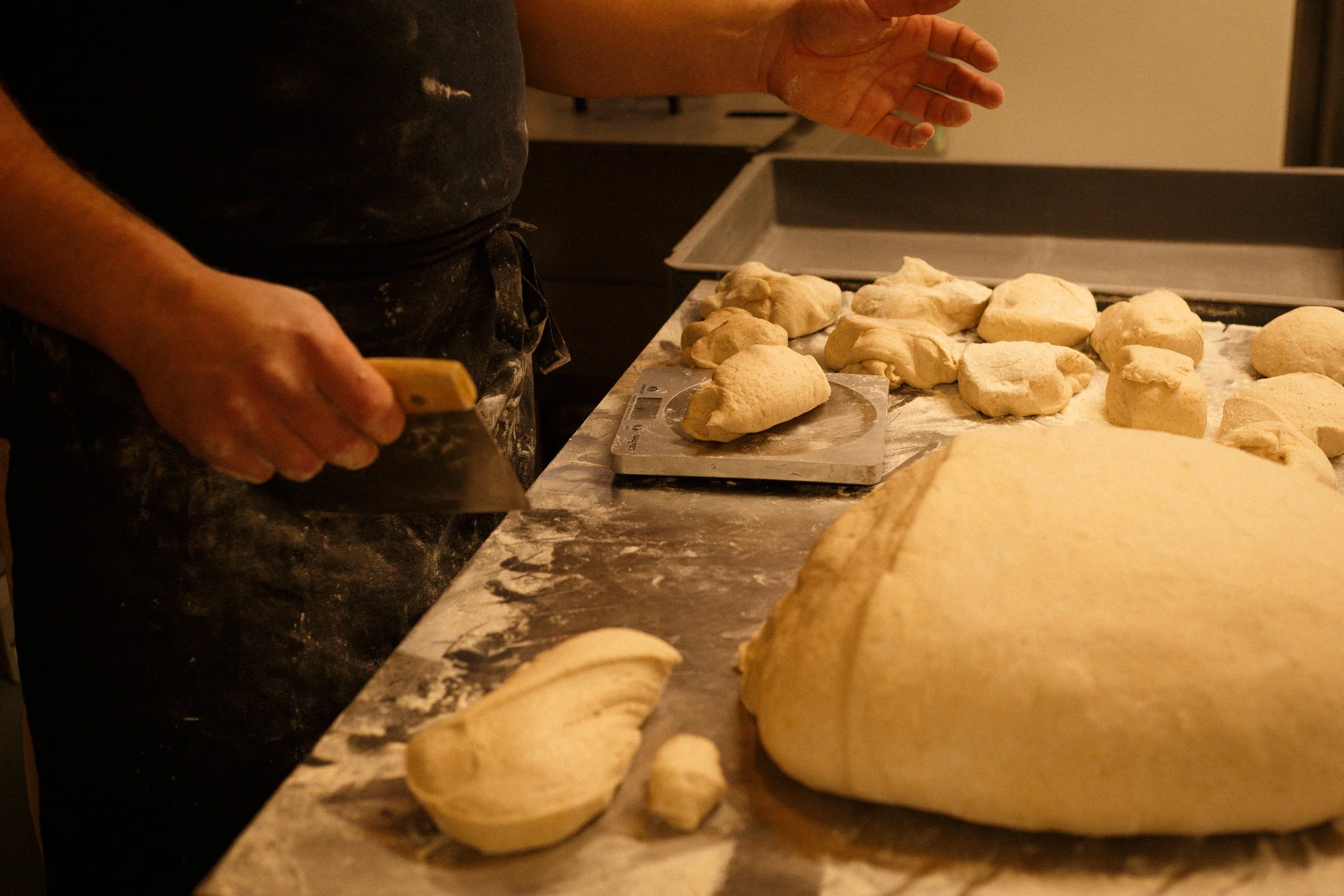 Person preparing bread dough on a floured countertop, with a large piece of dough and smaller shaped pieces around.
