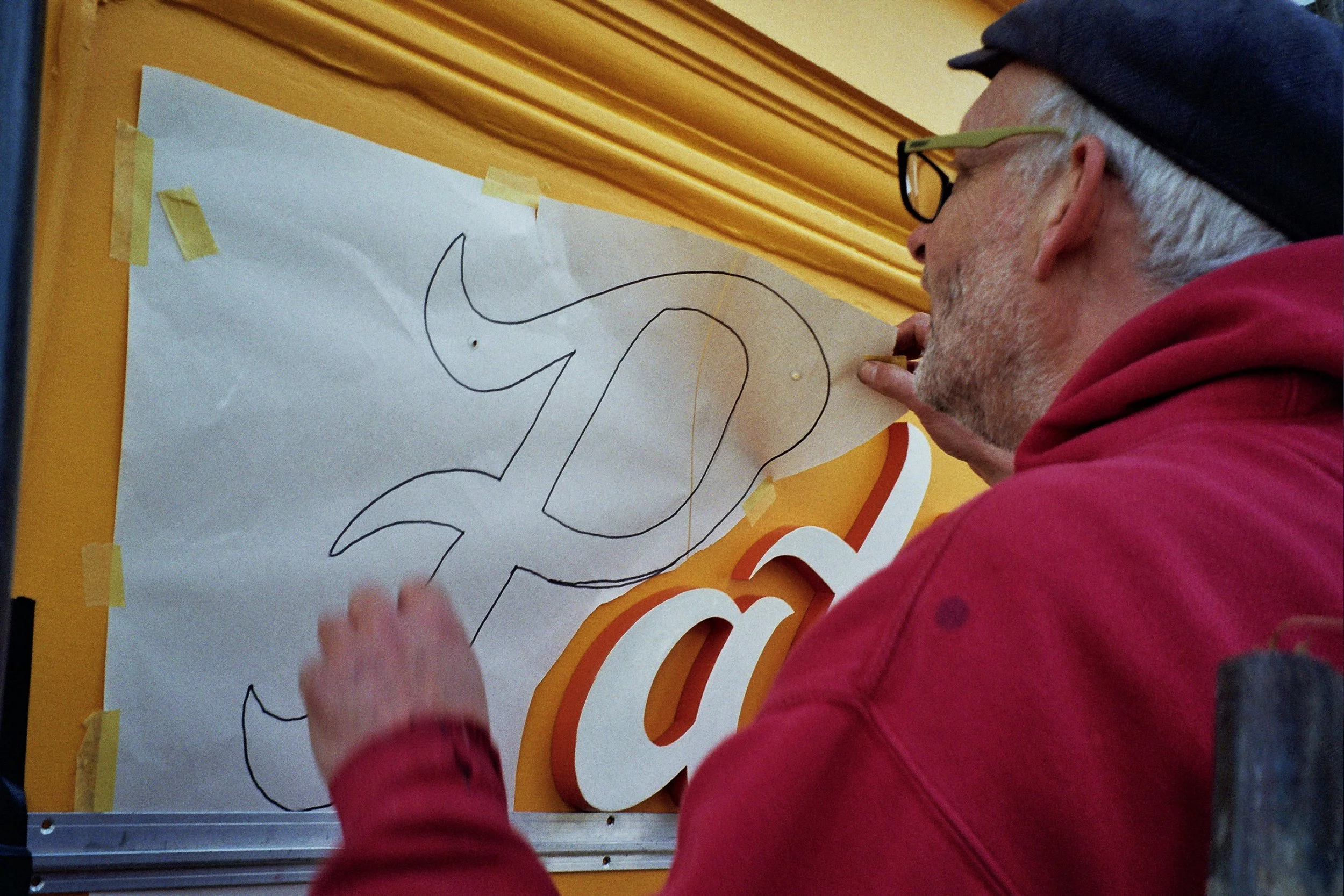 chris peeling the paper away to show where the holes need to be drilled on the P for the Pat's pizza sign