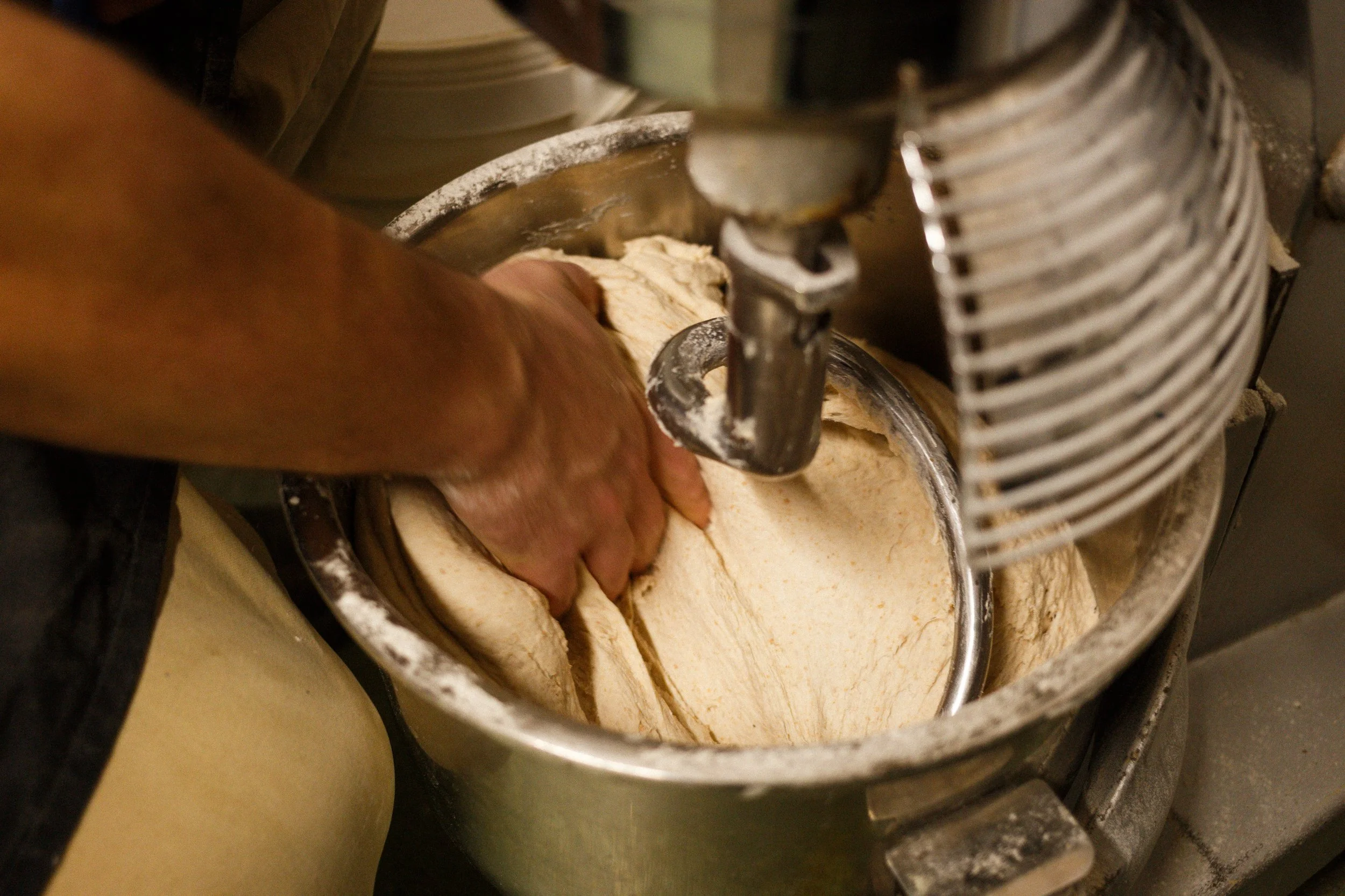 Person kneading dough in a stainless steel mixing bowl using a stand mixer.