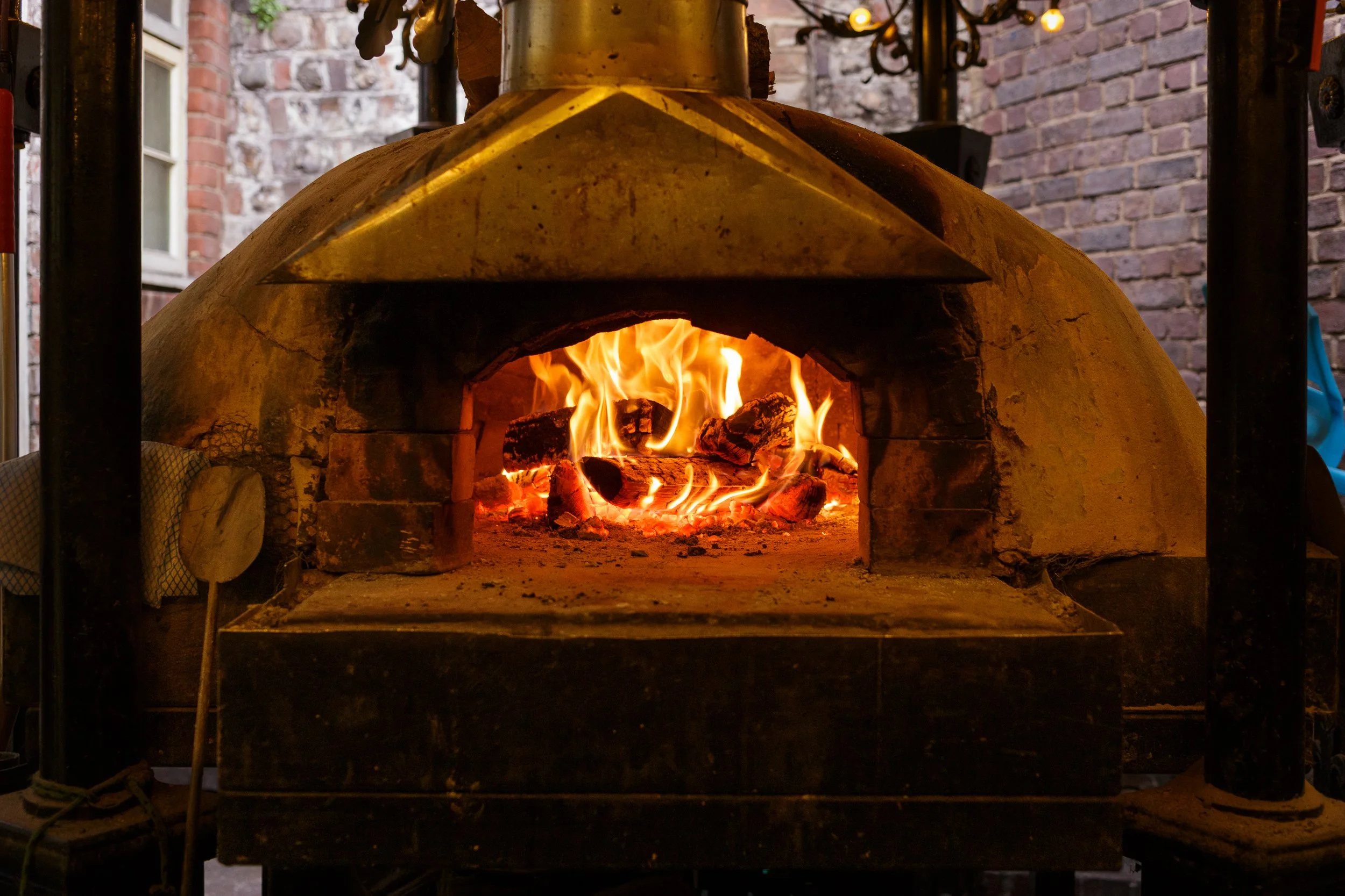 Our hand-built wood-fired brick oven, at The Lewes Arms pub in Lewes, with a glowing fire inside.