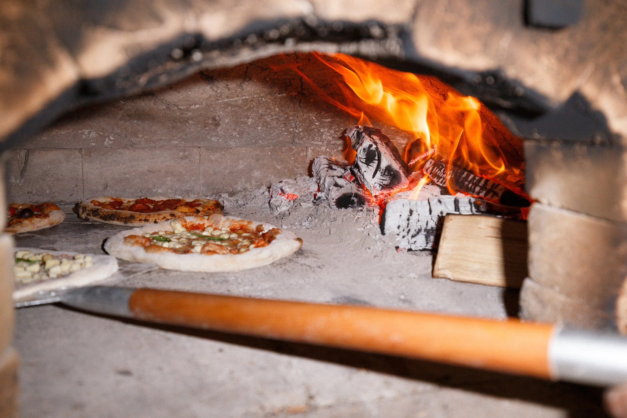 Pizza cooking in our hand-built wood-fired oven, at The Lewes Arms pub, with flames and ashes visible.