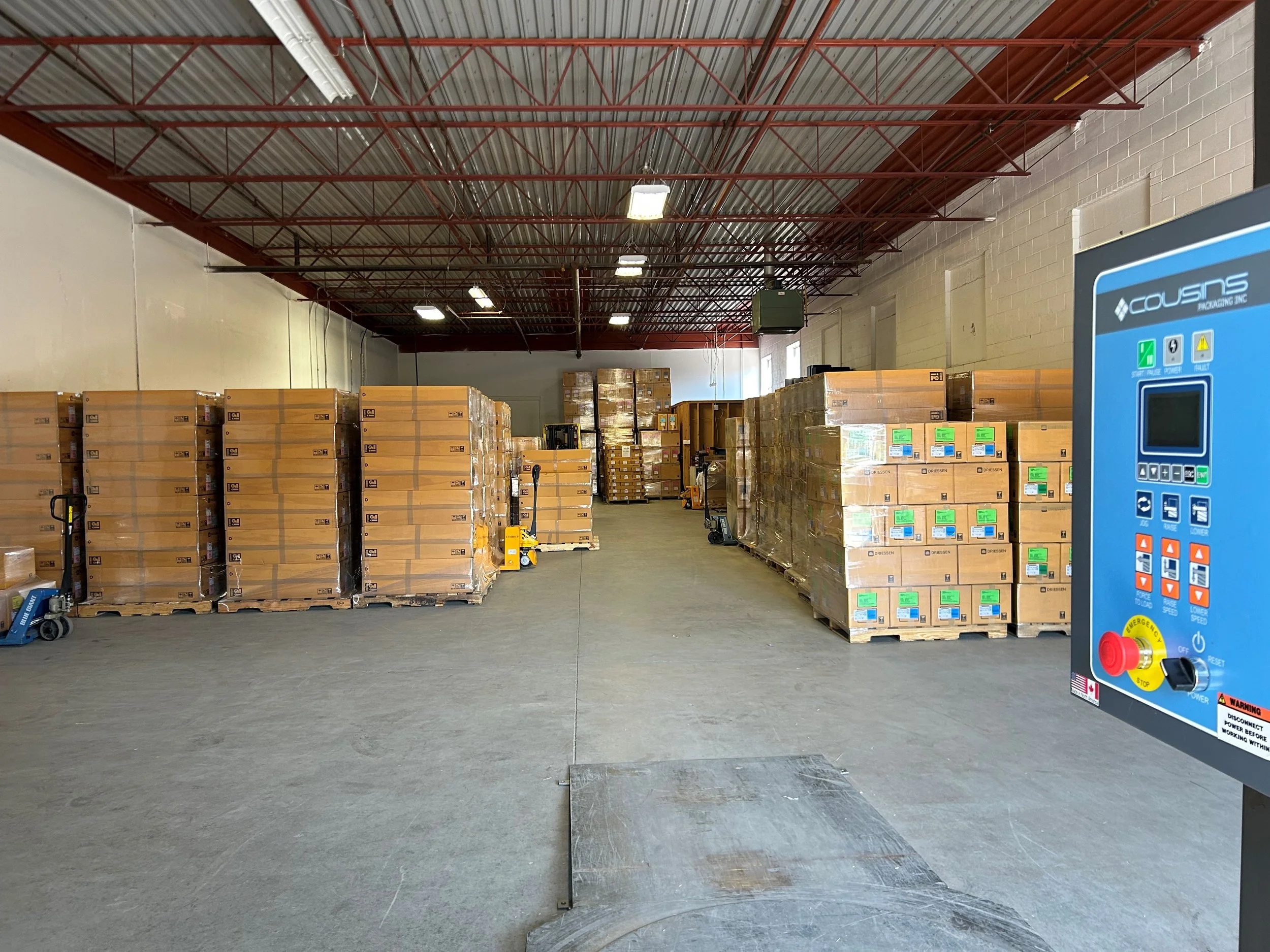 Warehouse with stacked boxes on pallets, a forklift, and a large blue control panel on the right.
