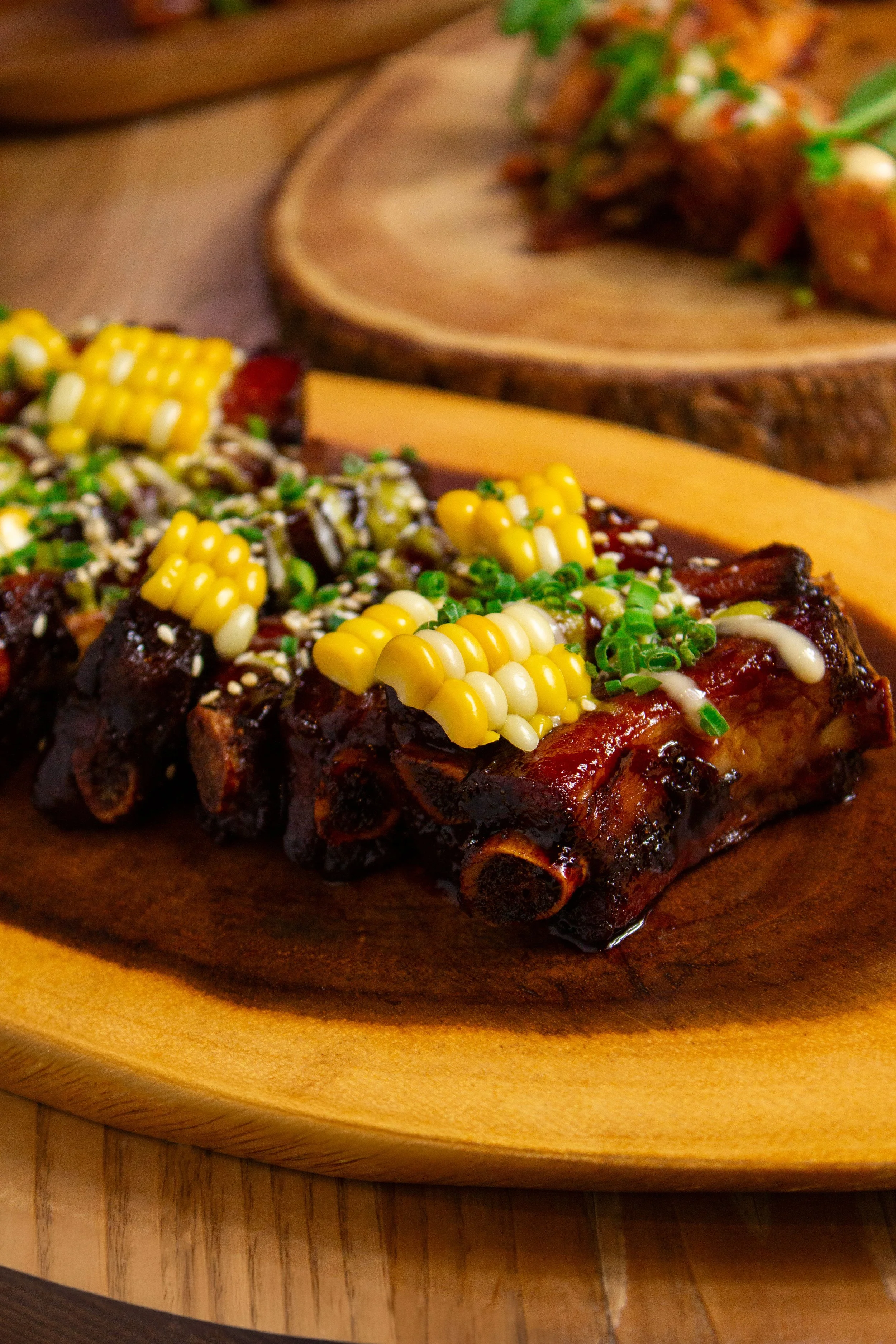 Barbecue ribs topped with yellow and white corn kernels and chopped green onions, served on a wooden platter with sliced green onions in the background.