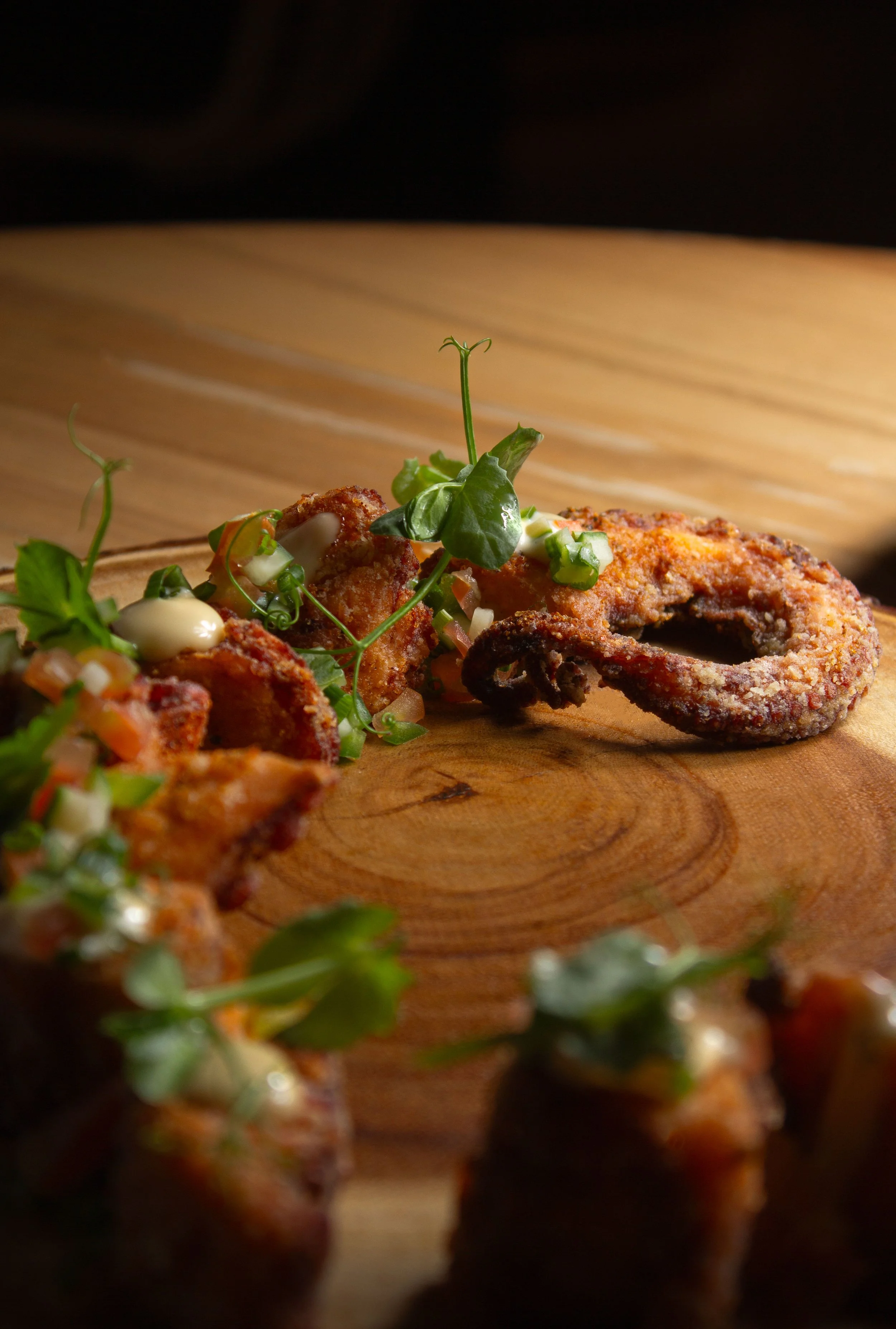 Fried calamari with green herbs and a creamy dipping sauce on a wooden serving board.