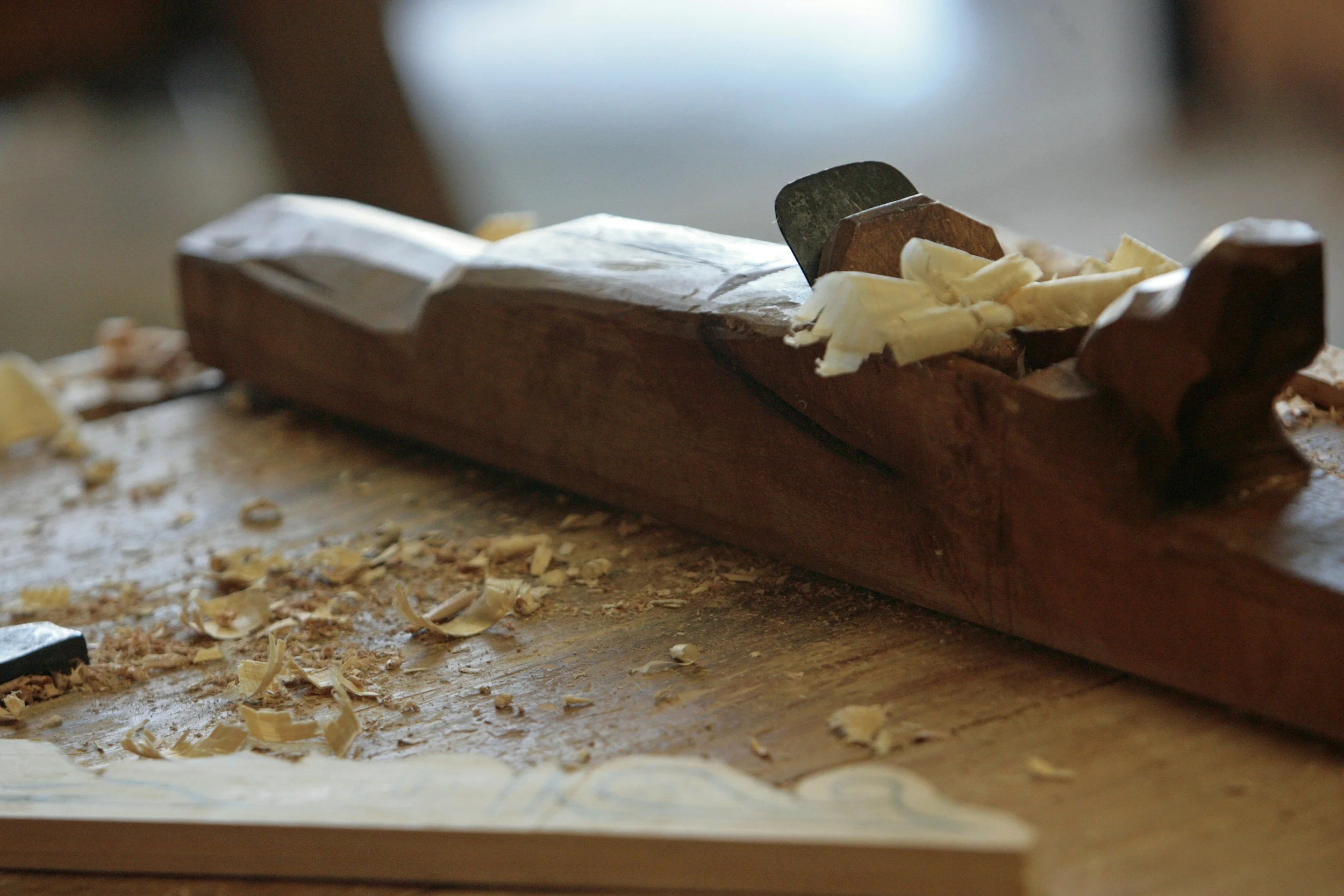 Close-up of a woodworking plane tool on a wooden workbench with wood shavings scattered around.