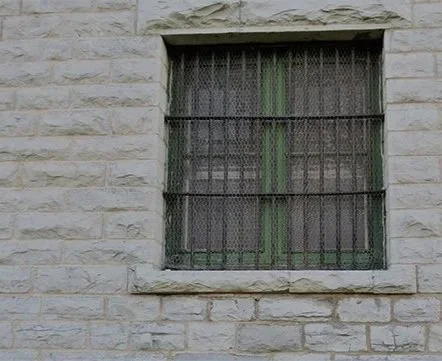 A brick building with a barred window and a thin black security bar across it.