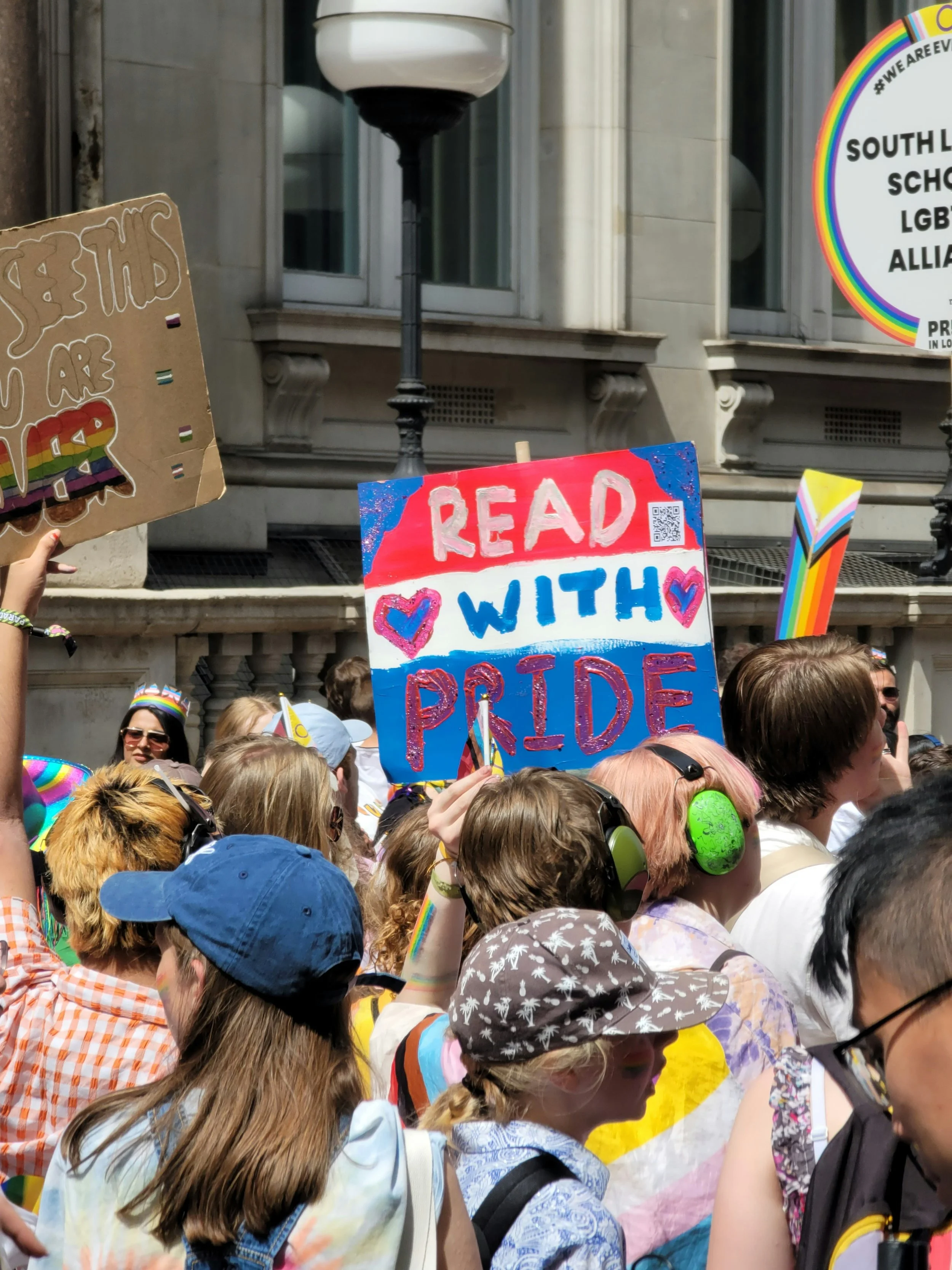 Person holding a "Read With Pride" sign at a march. Photo by Wayee Tan on Unspalsh.