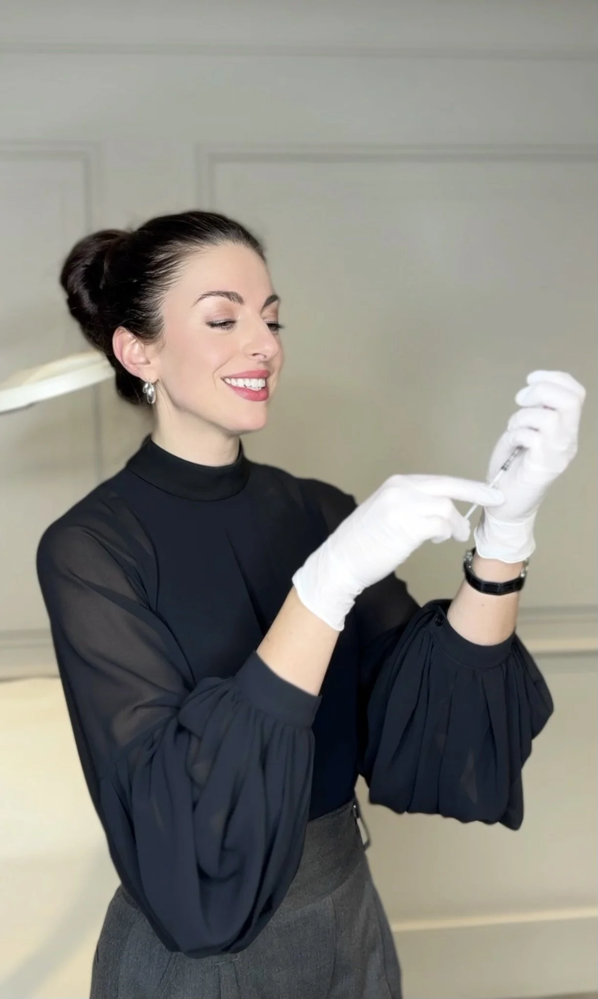 A woman smiling and preparing a syringe with gloves on, in a professional setting.