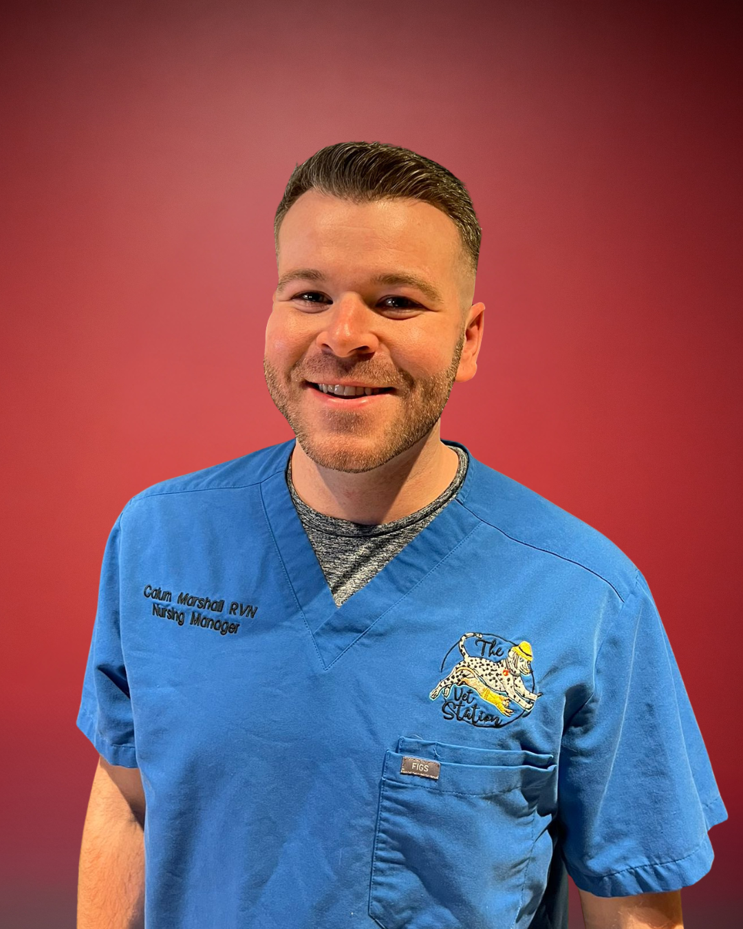 A man wearing scrubs and a colorful surgical cap, smiling at the camera, with a stethoscope around his neck, in a room with a blue towel or cloth and electrical outlets on the wall.