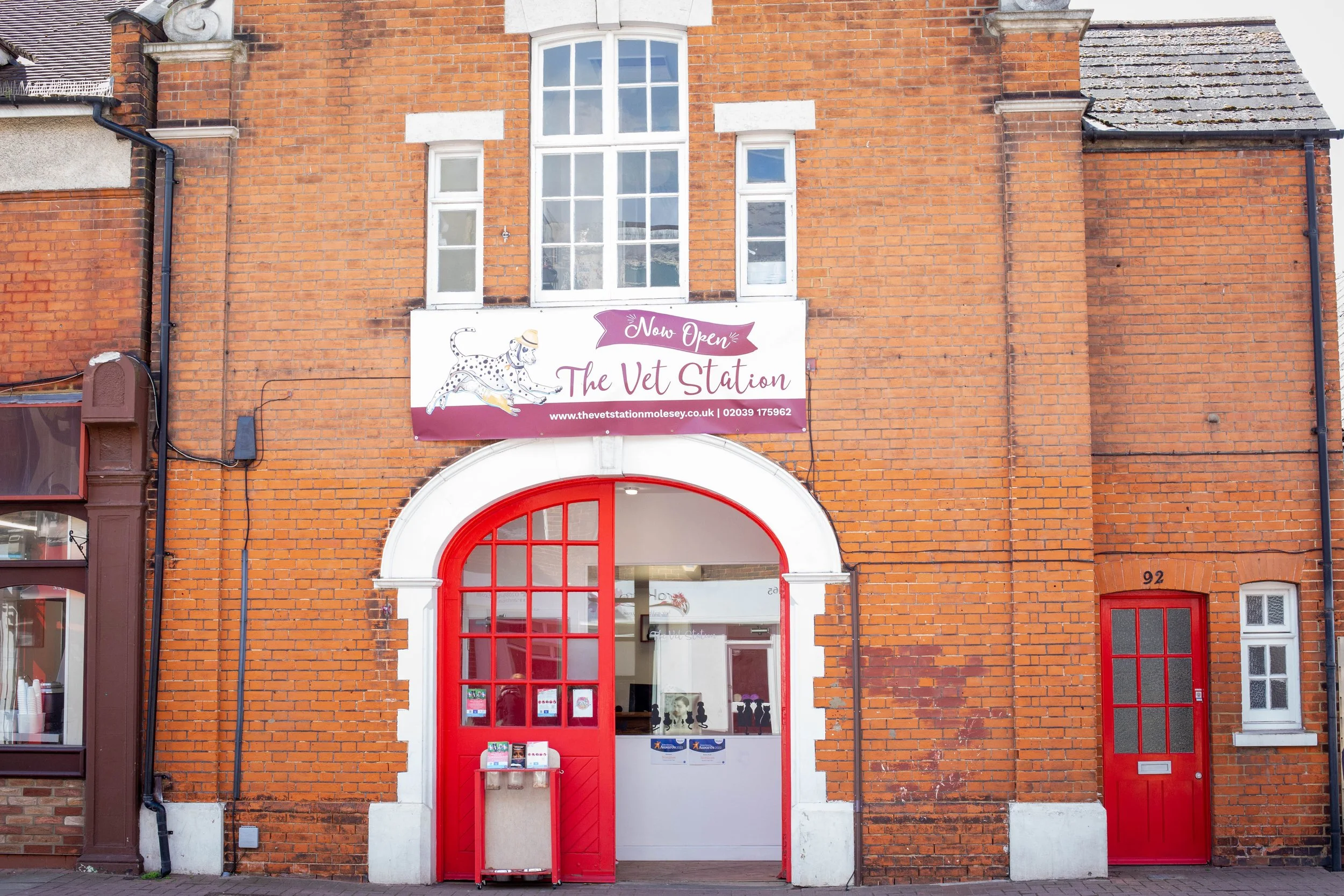 Brick building with a veterinary clinic called 'The Vet Station' with a purple and white sign, red doors, and a large arched entrance.