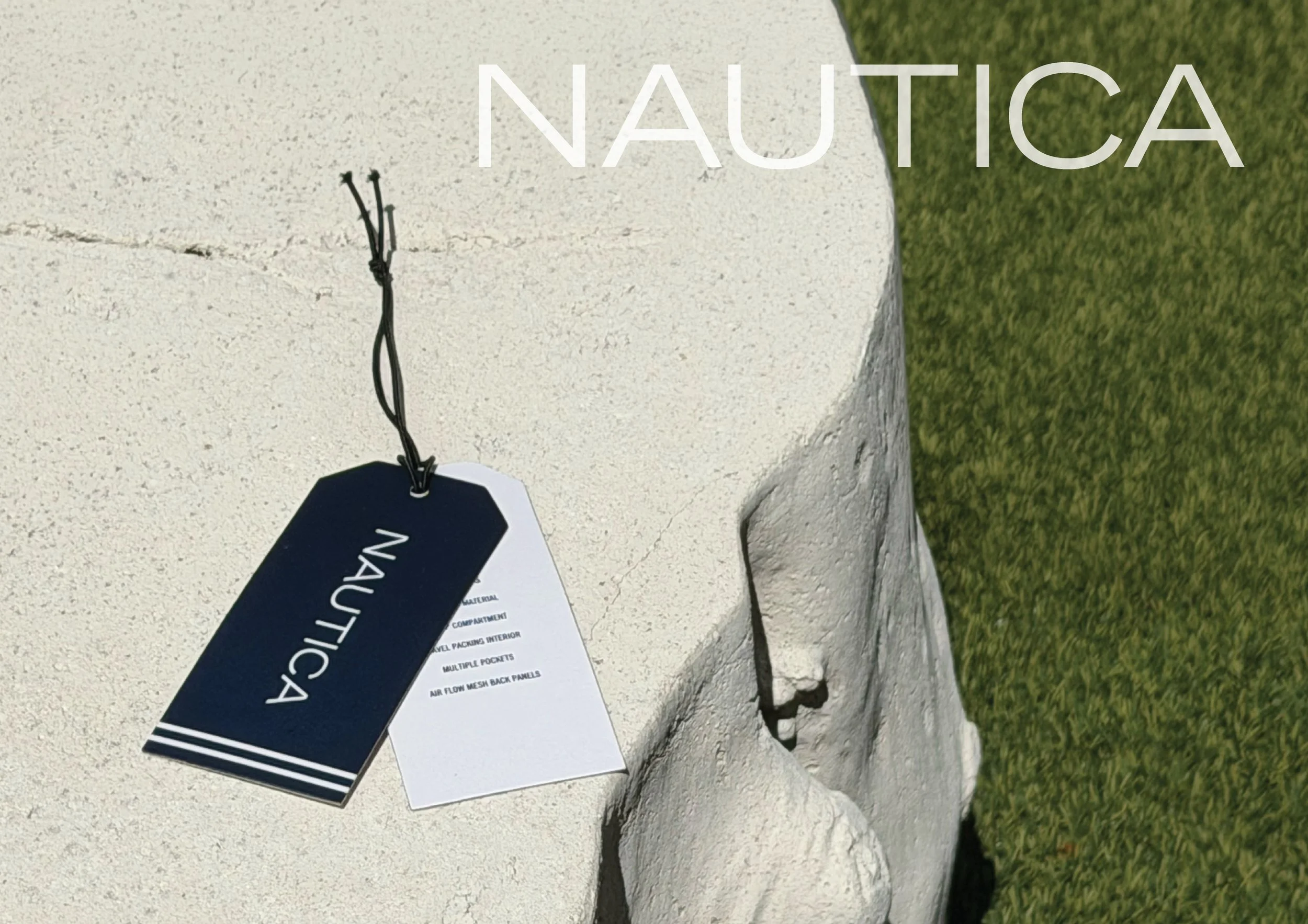 Close-up photograph of a white stone sculpture with a black and white NAUTICA tag attached, set outdoors on a grassy surface.