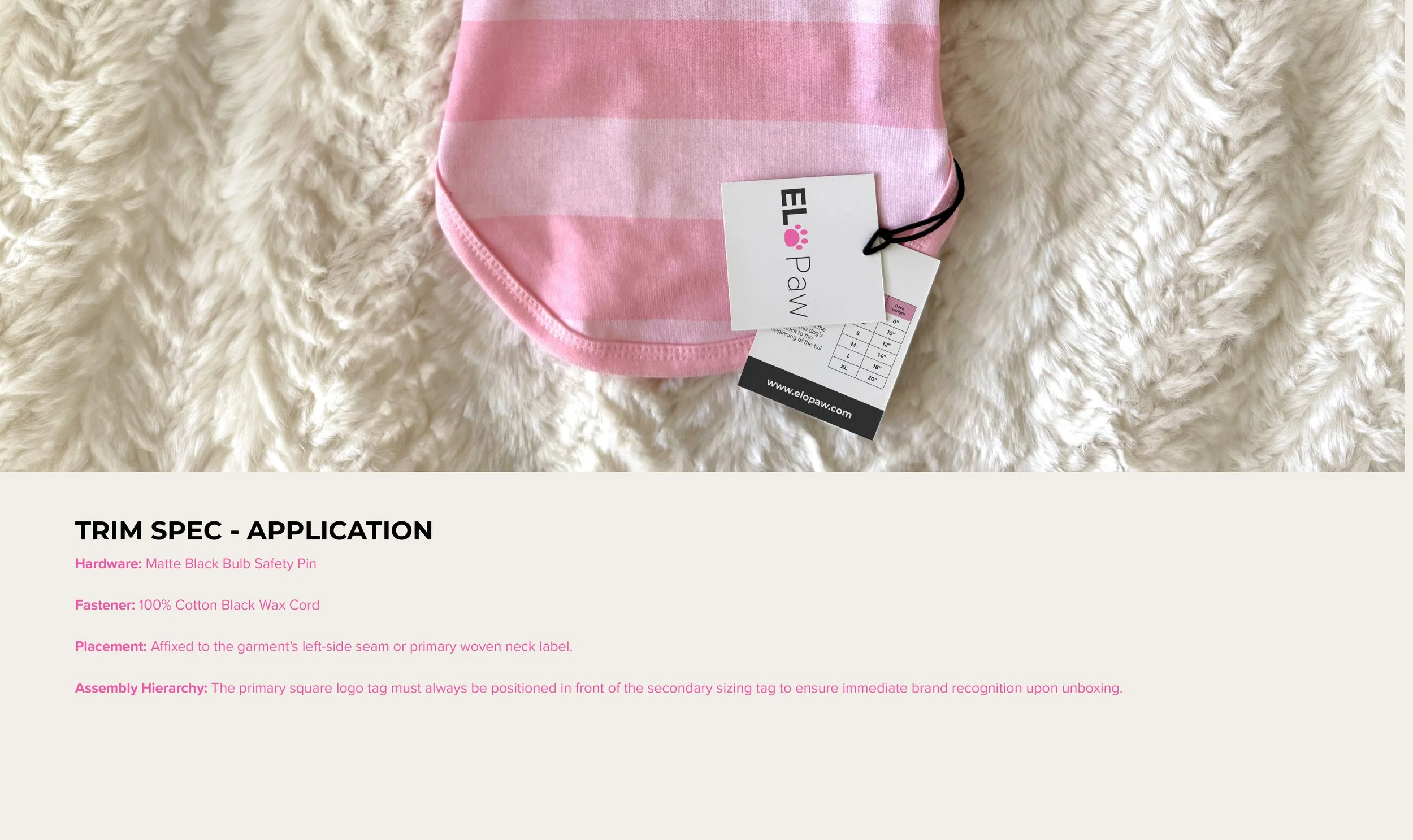 A pink, striped cloth face mask placed on a white, fluffy surface with a tag attached that reads 'ELLA Paw' and includes sizing information.
