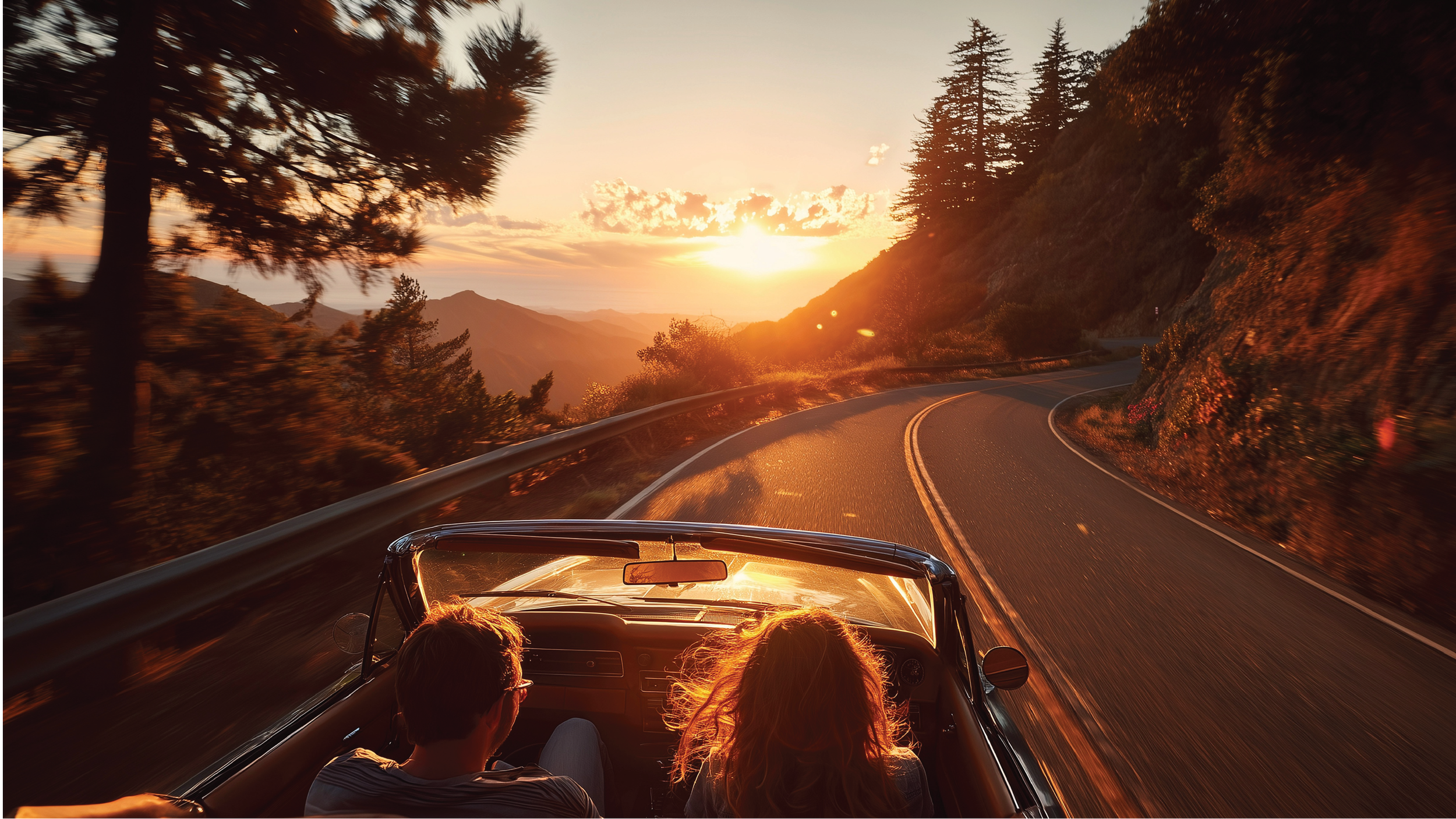 A convertible car with two passengers, a man and a woman, driving on a winding mountain road at sunset, with trees on either side and mountains in the background.