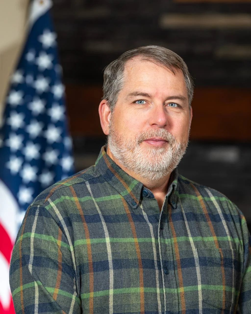 Portrait of congressional candidate Johnn Duresky, wearing a plaid shirt, standing in front of an American flag.