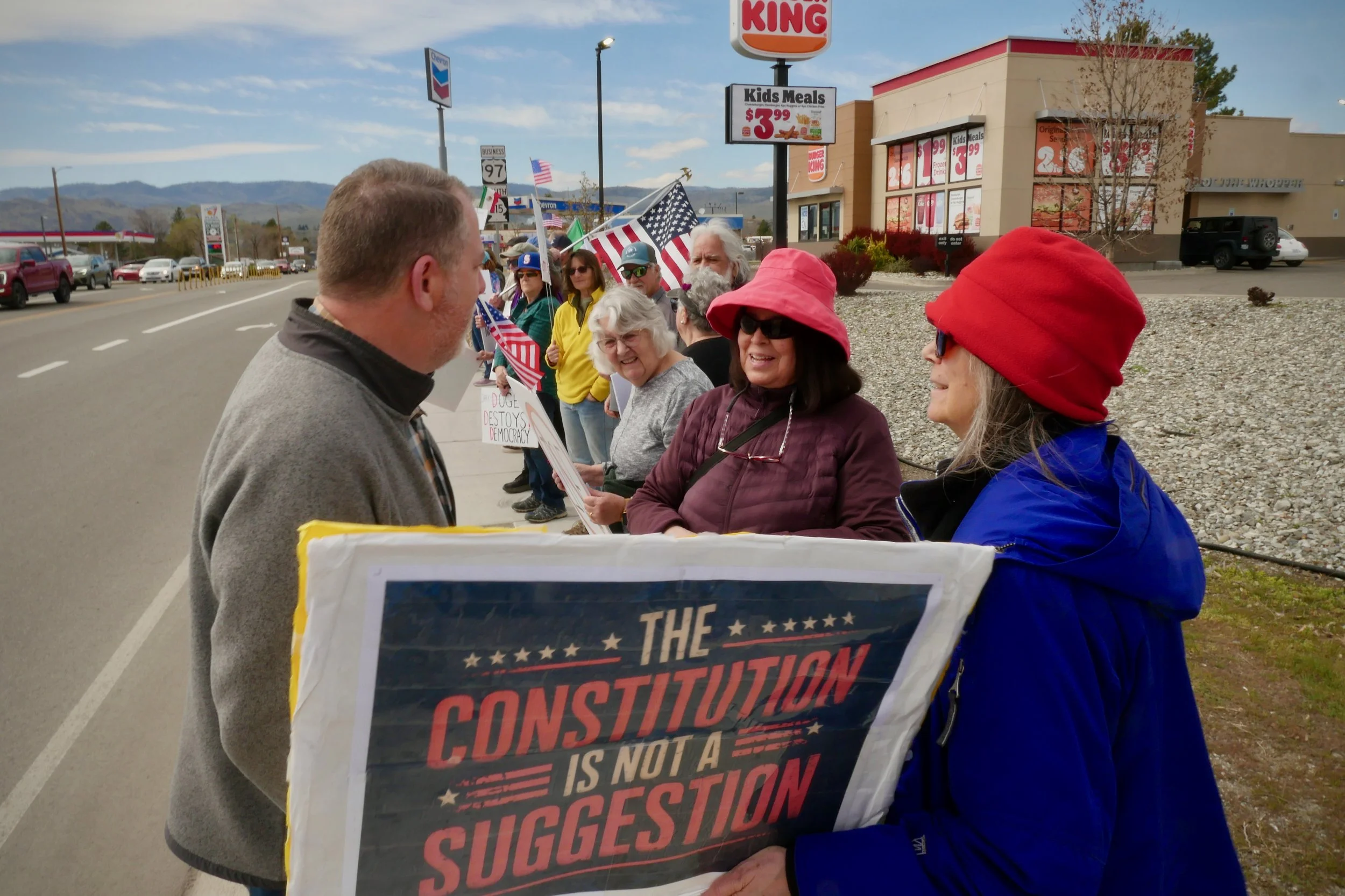 A group of people at a NO KINGS protest on sidewalk in Omake, WA, holding American flags and signs talking with congressional candidate, John Duresky.