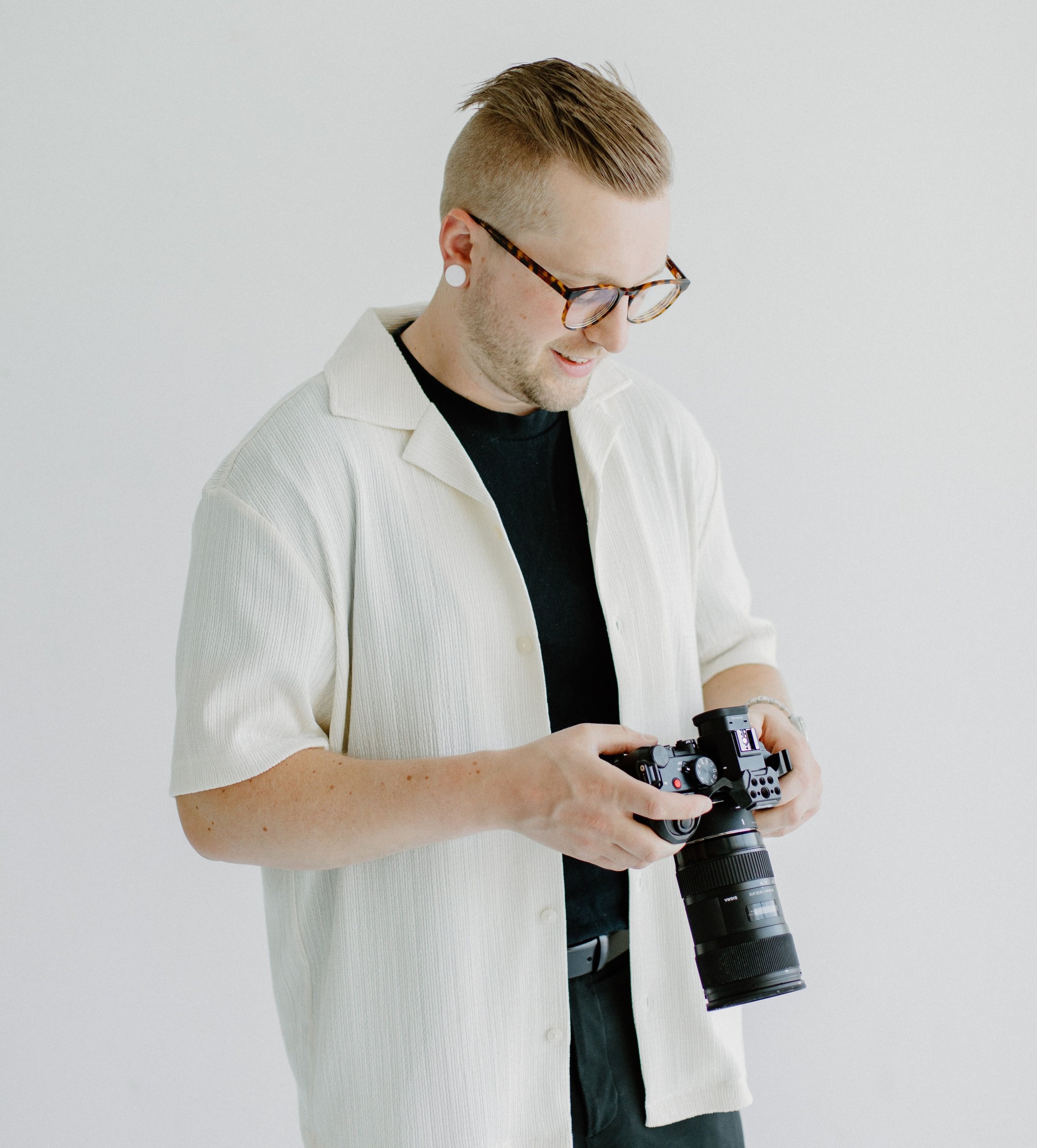 A man with glasses holding a camera, looking down towards it's screen